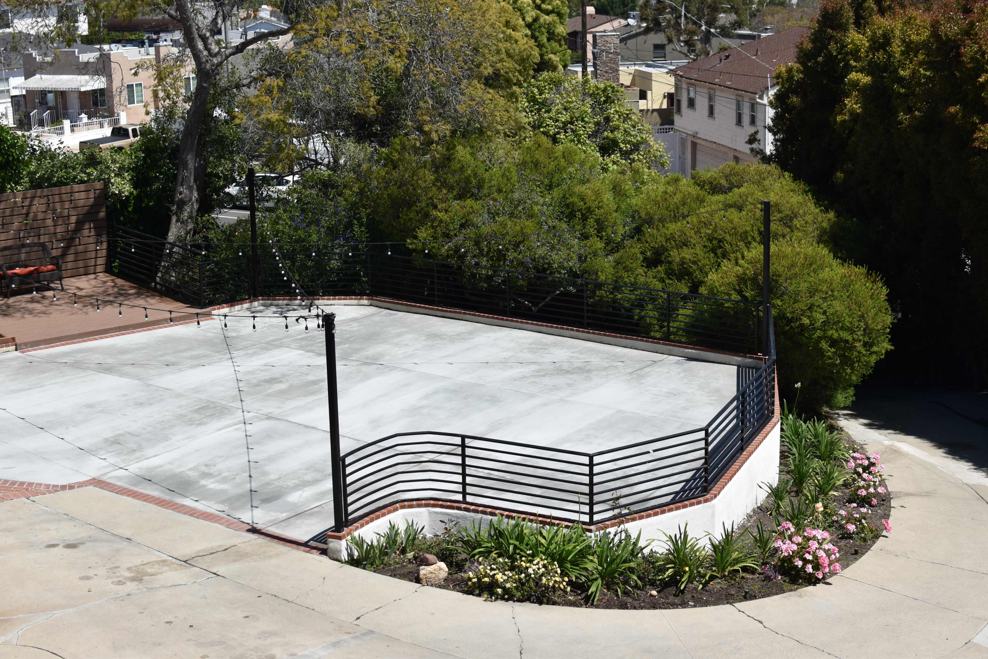 A concrete parking area surrounded by greenery and a wire fence on a sloped property.