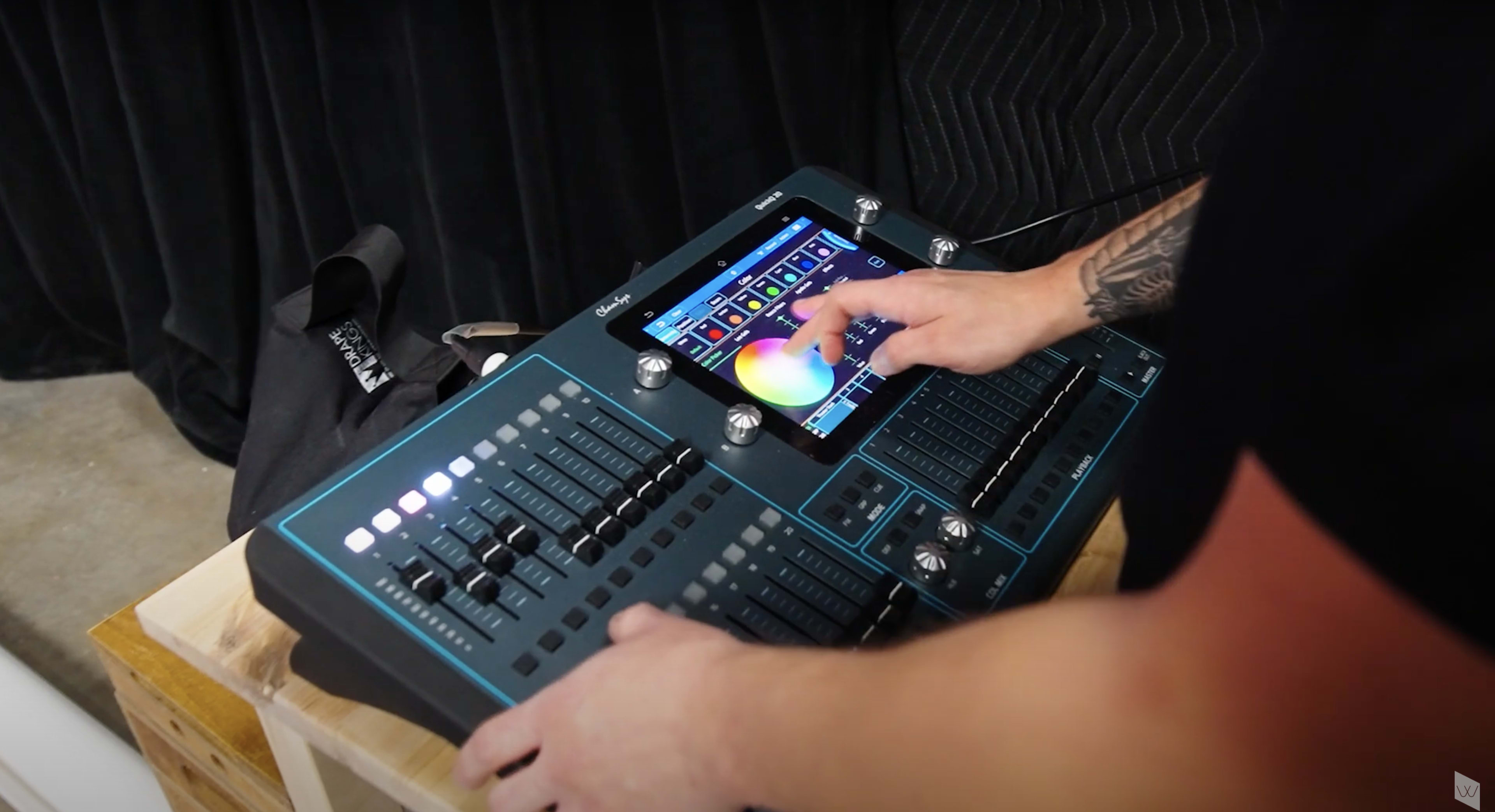 A person uses a digital mixing console with touchscreen controls and various sliders and knobs.
