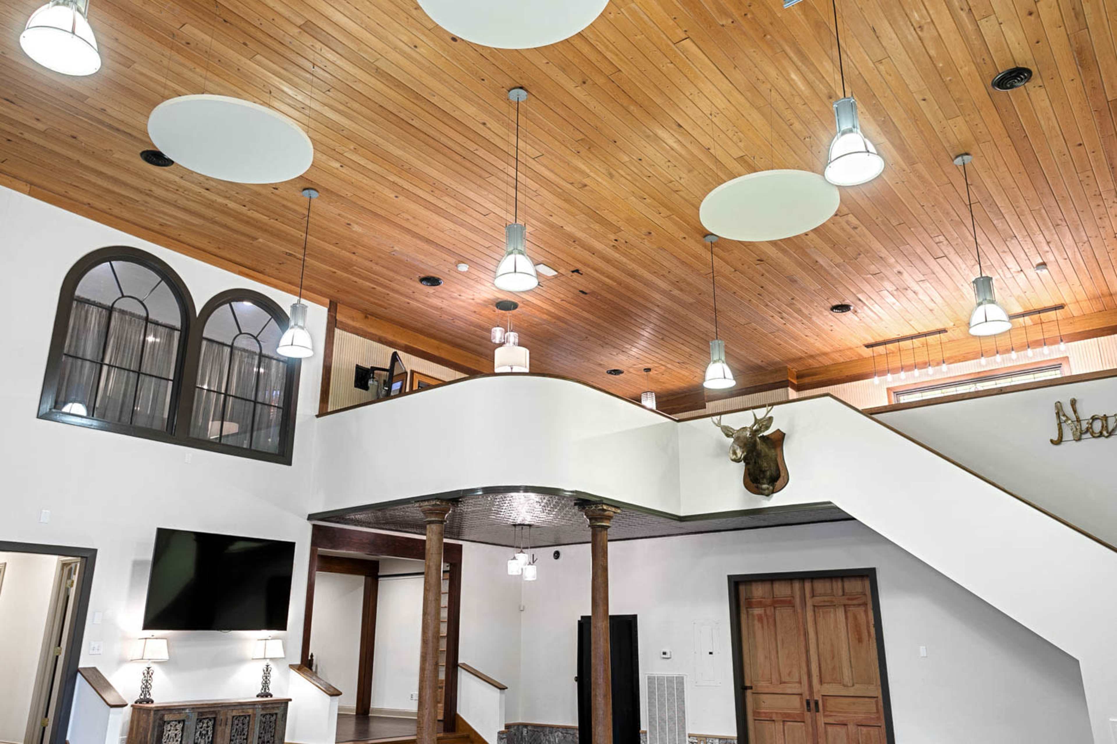 The image shows a spacious interior with a wooden ceiling, modern light fixtures, and a staircase leading to an upper level.