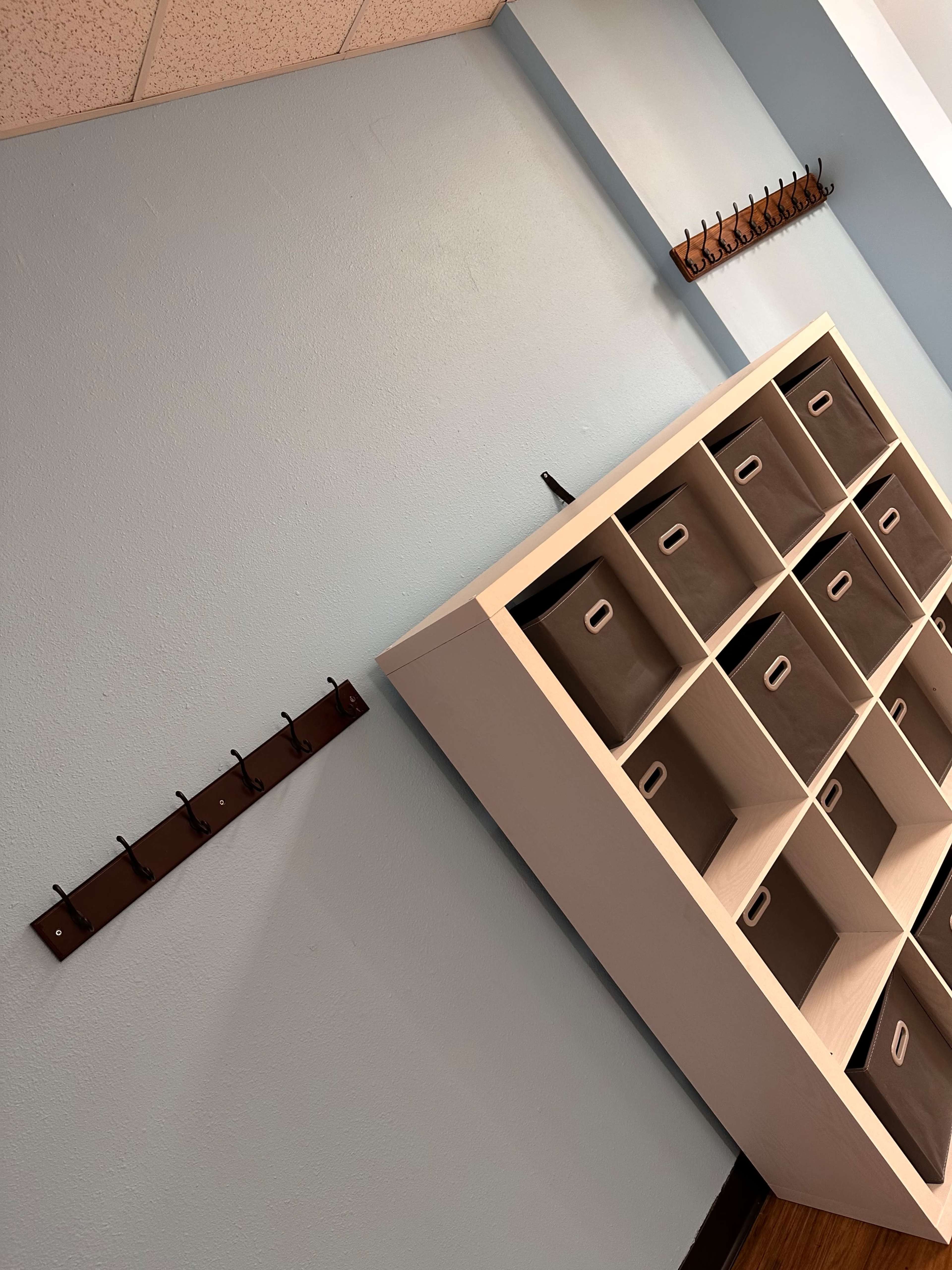 The image shows a light blue wall with a pegboard and a storage unit featuring several gray fabric bins.