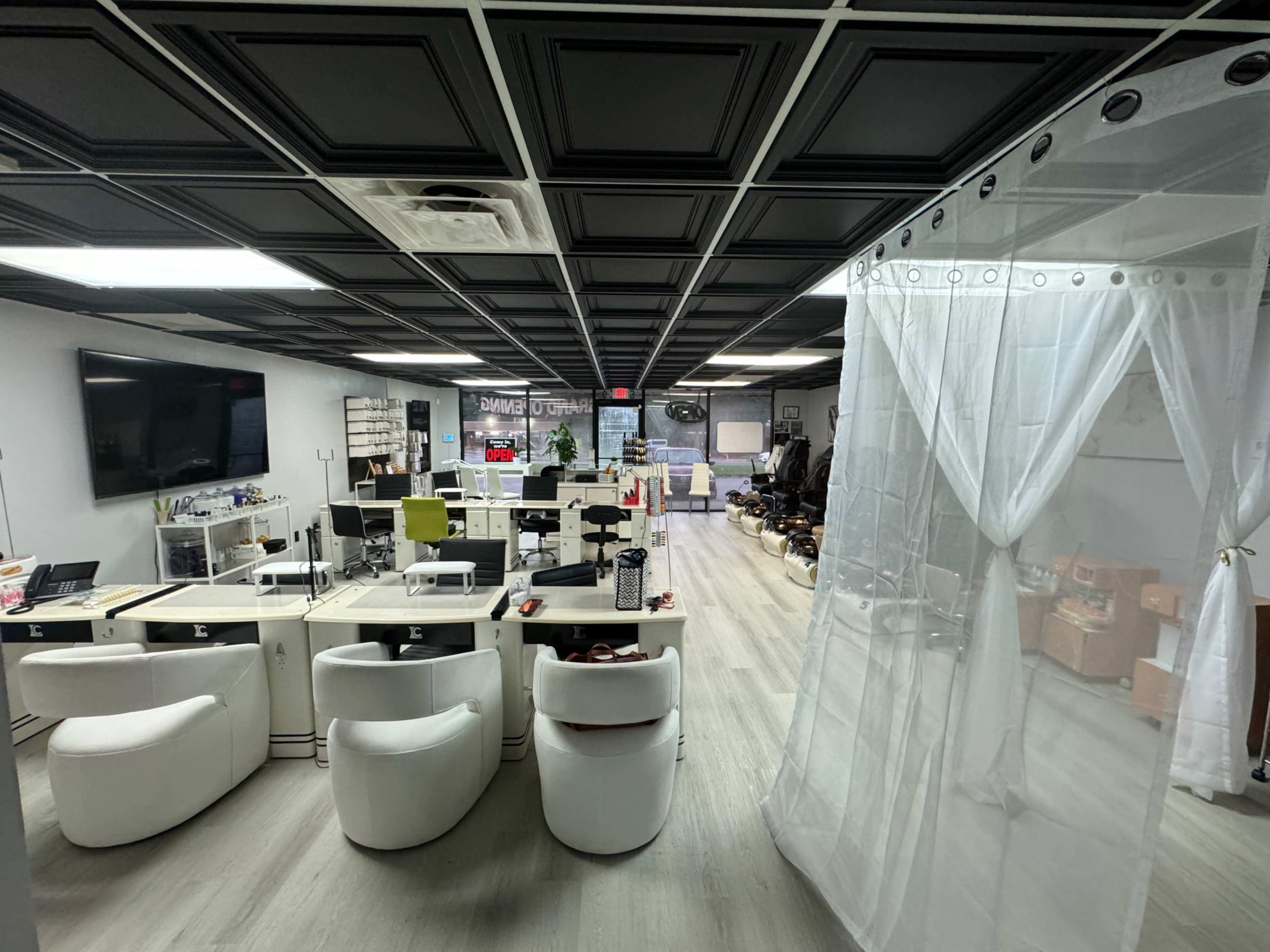 The image shows a modern office space featuring white furniture, a large television, and a transparent curtain dividing areas of the room.