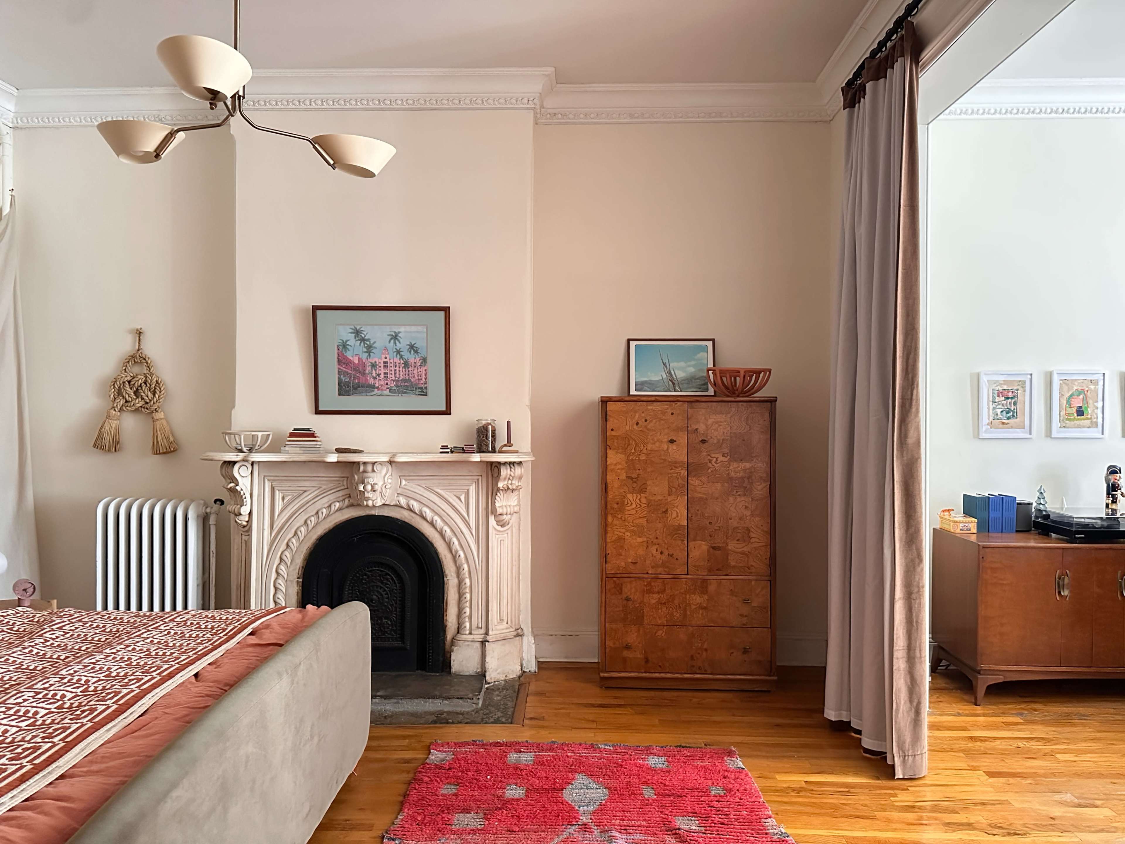 The image shows a cozy bedroom featuring a decorative fireplace, wooden furniture, and a pink rug on a hardwood floor.