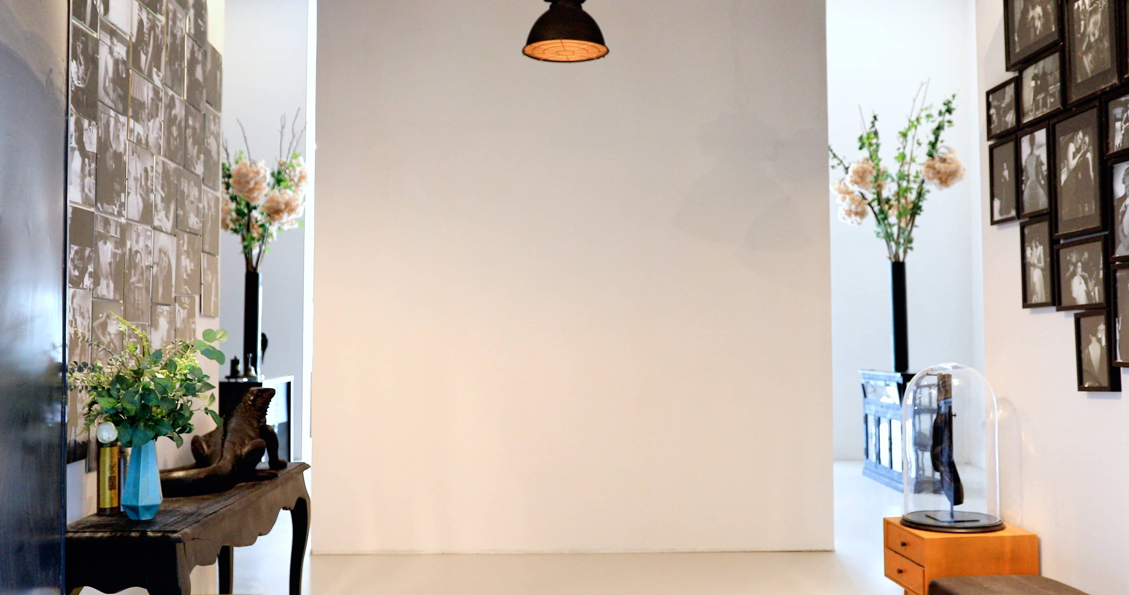 A minimalist hallway featuring a black and white photo collage on one wall, a small table with a plant, and tall vases with flowers on either side.