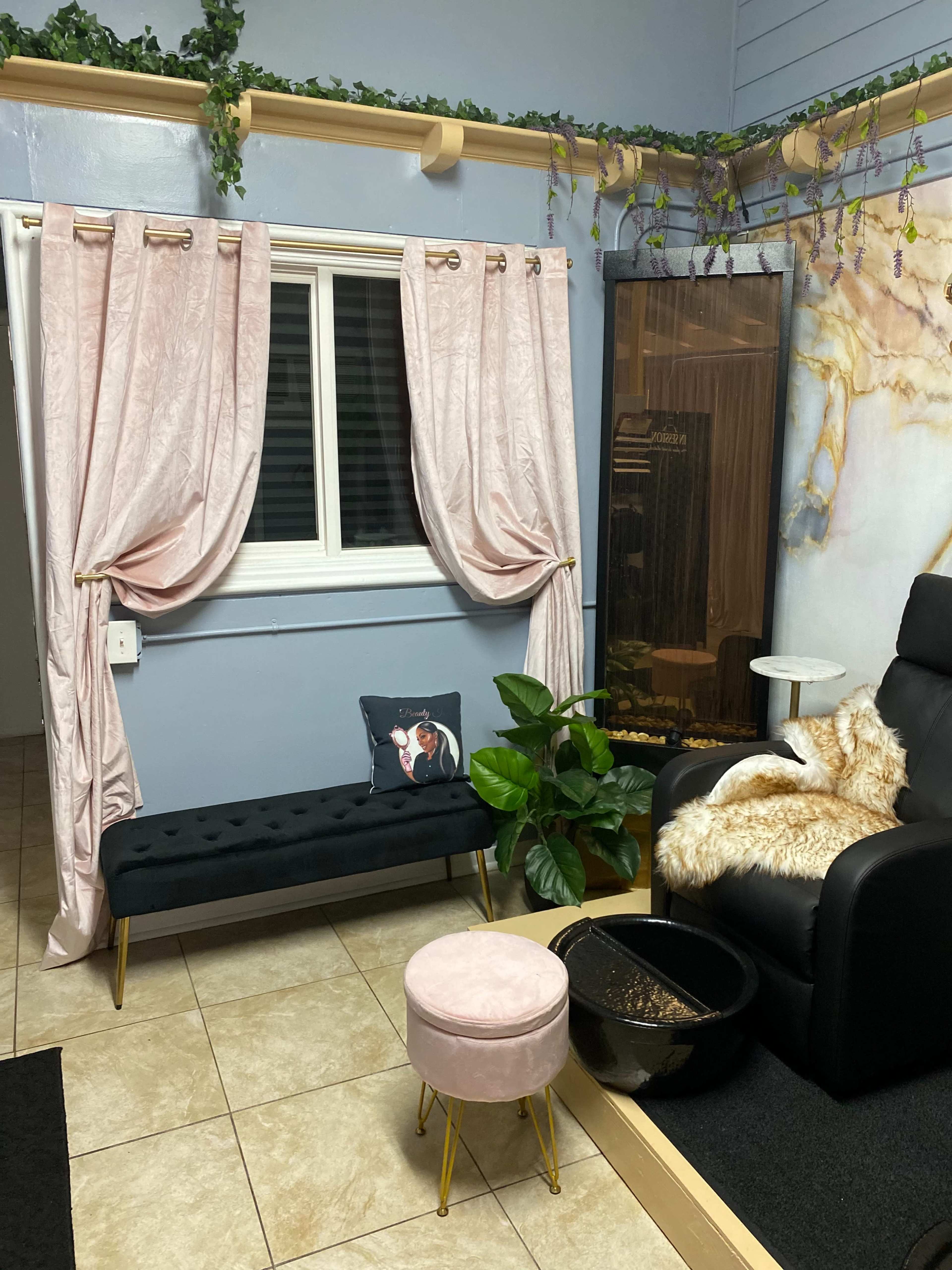 A cozy indoor corner featuring a black bench with gold legs, a pink stool, a black recliner, and curtains draping over a window, surrounded by a potted plant and decor.