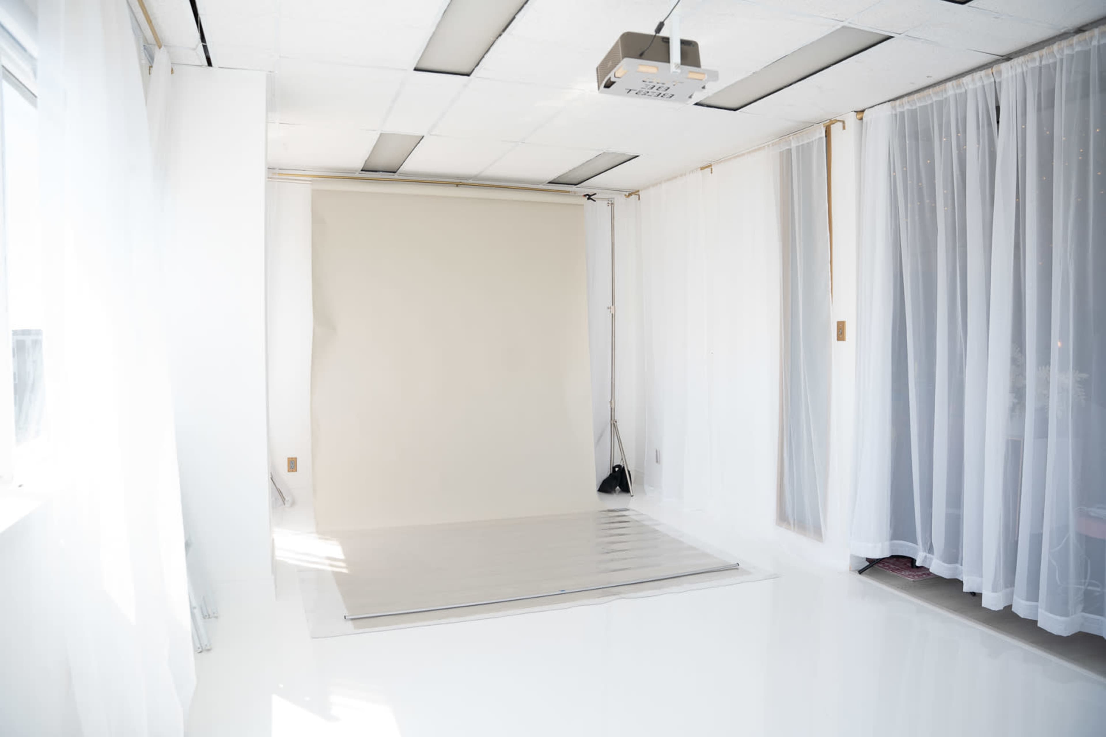The image shows a bright, empty photography studio featuring a smooth, light-colored backdrop and sheer white curtains.