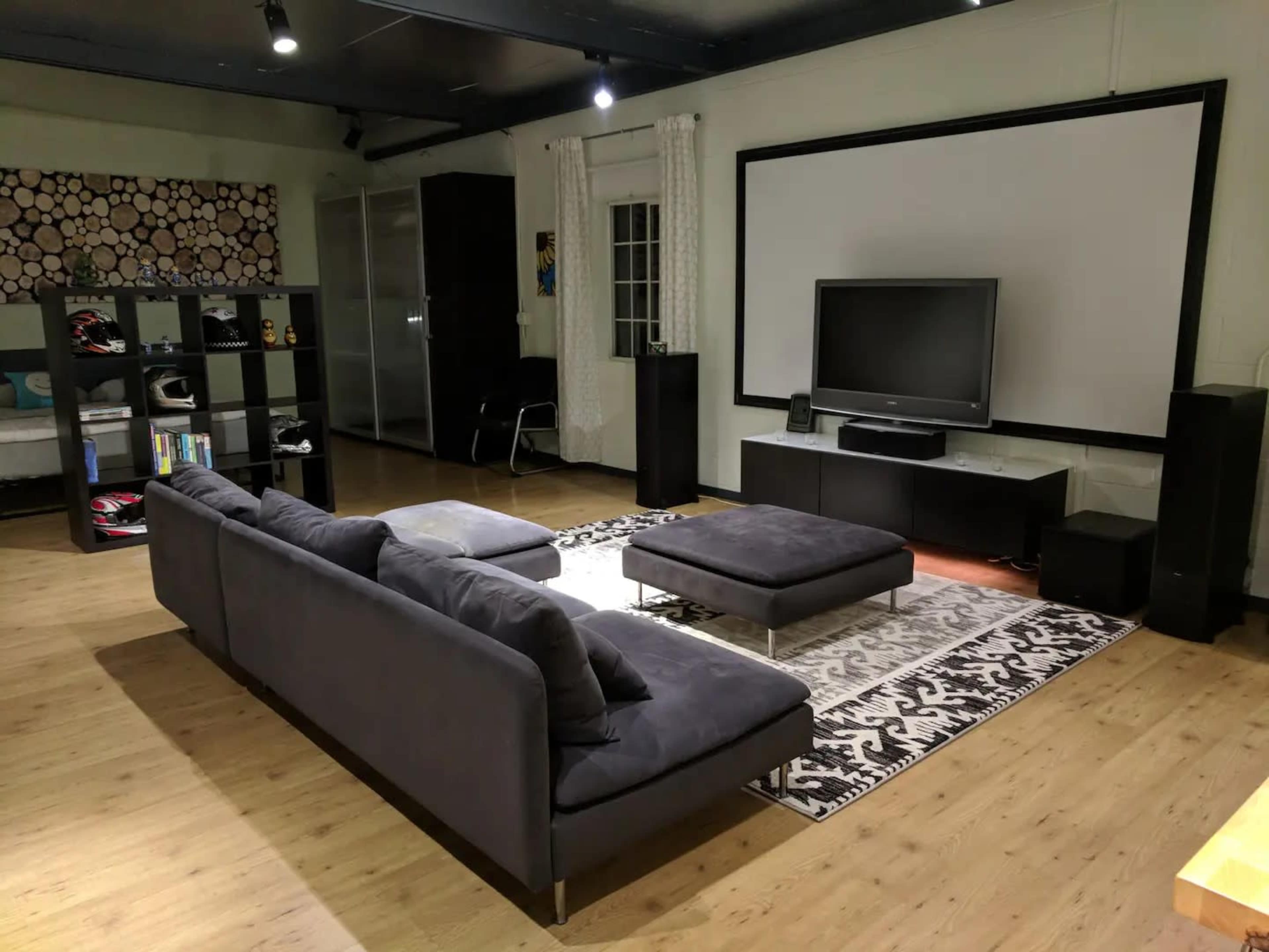 A modern living room features a sectional sofa, a large flat-screen TV on a low console, and a patterned rug on a wooden floor.