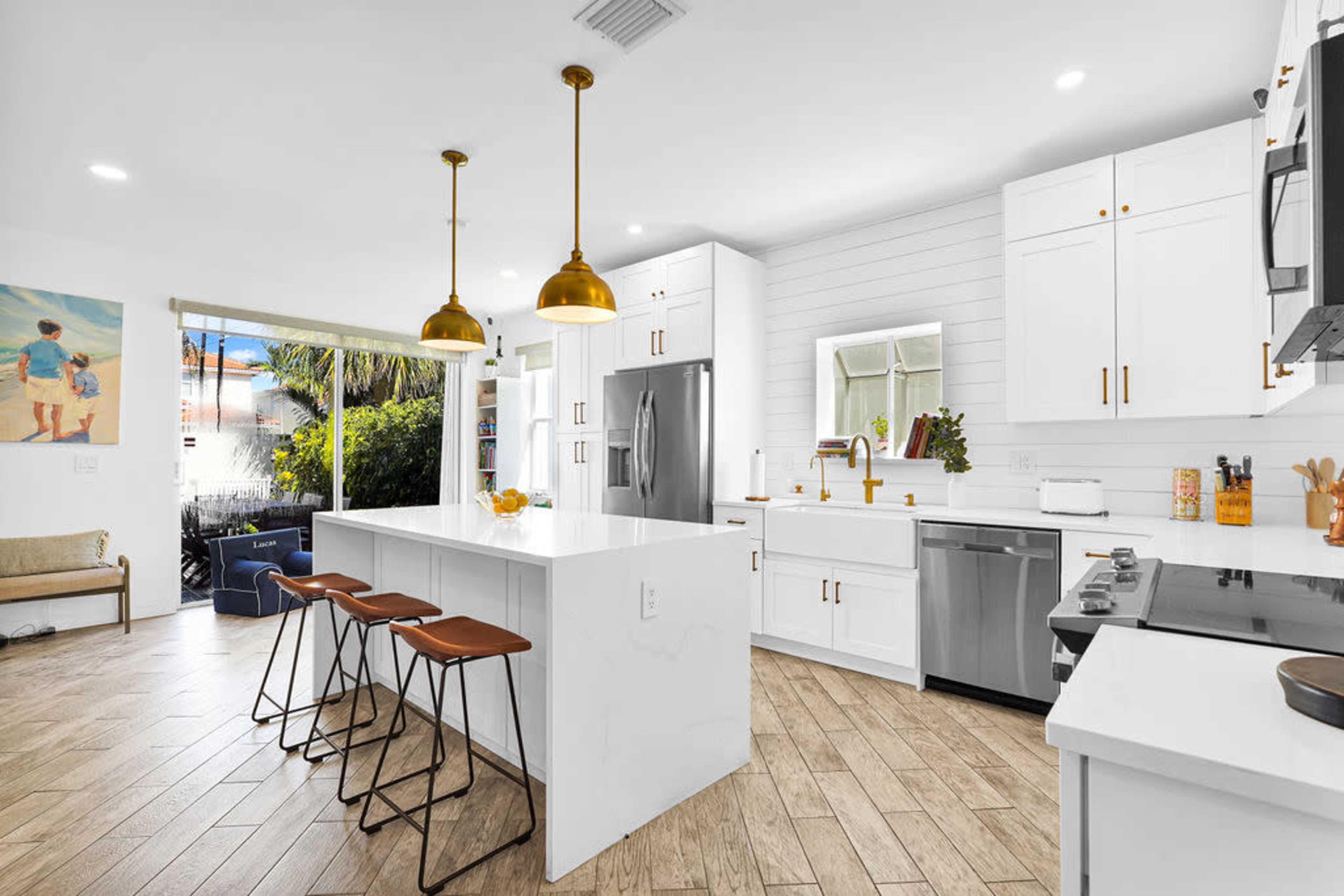 The kitchen features white cabinetry, a large island with three bar stools, and gold pendant lights, creating a modern and open layout.