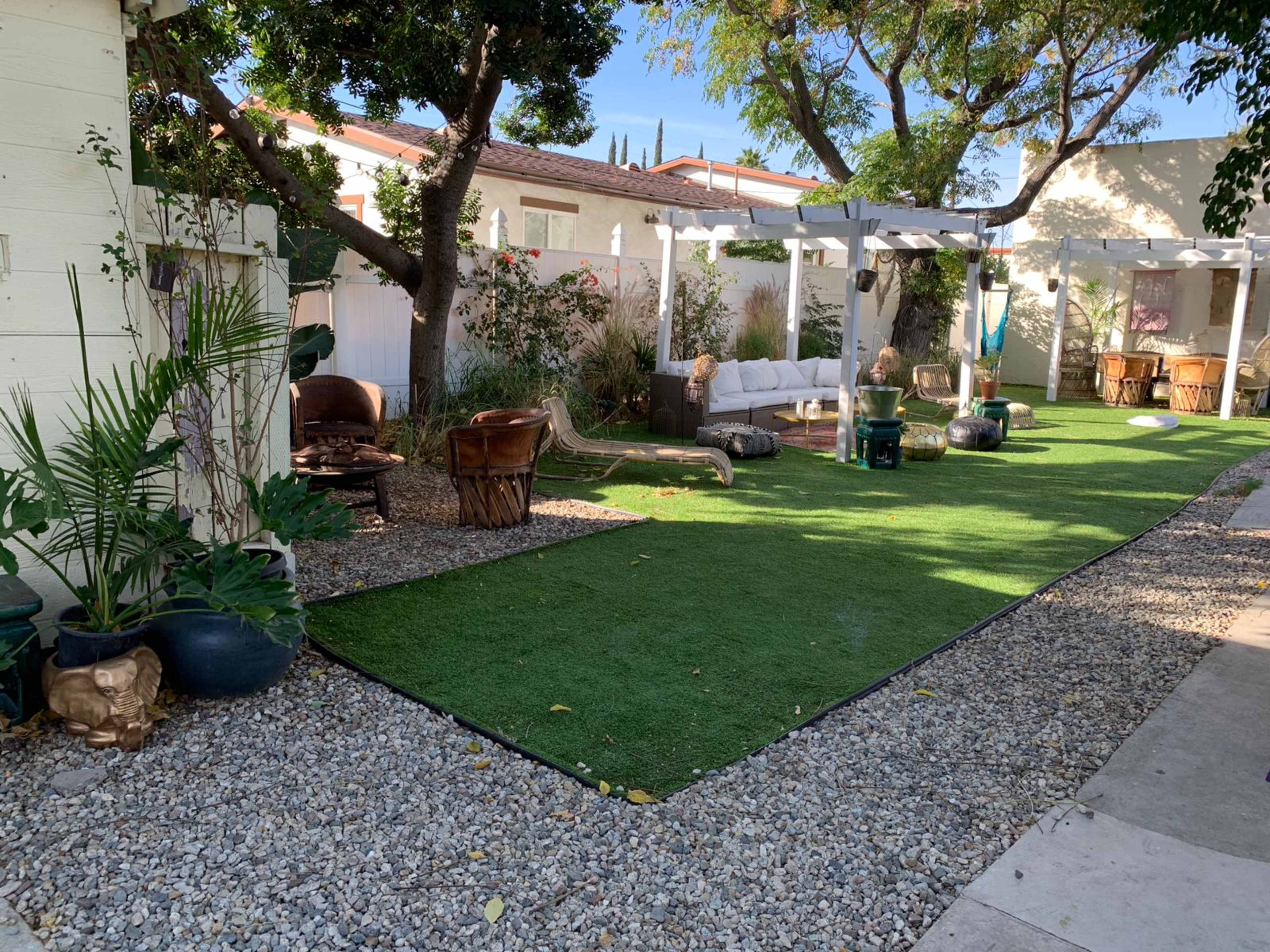 A landscaped outdoor area featuring artificial grass, decorative stones, and seating arrangements under trees.