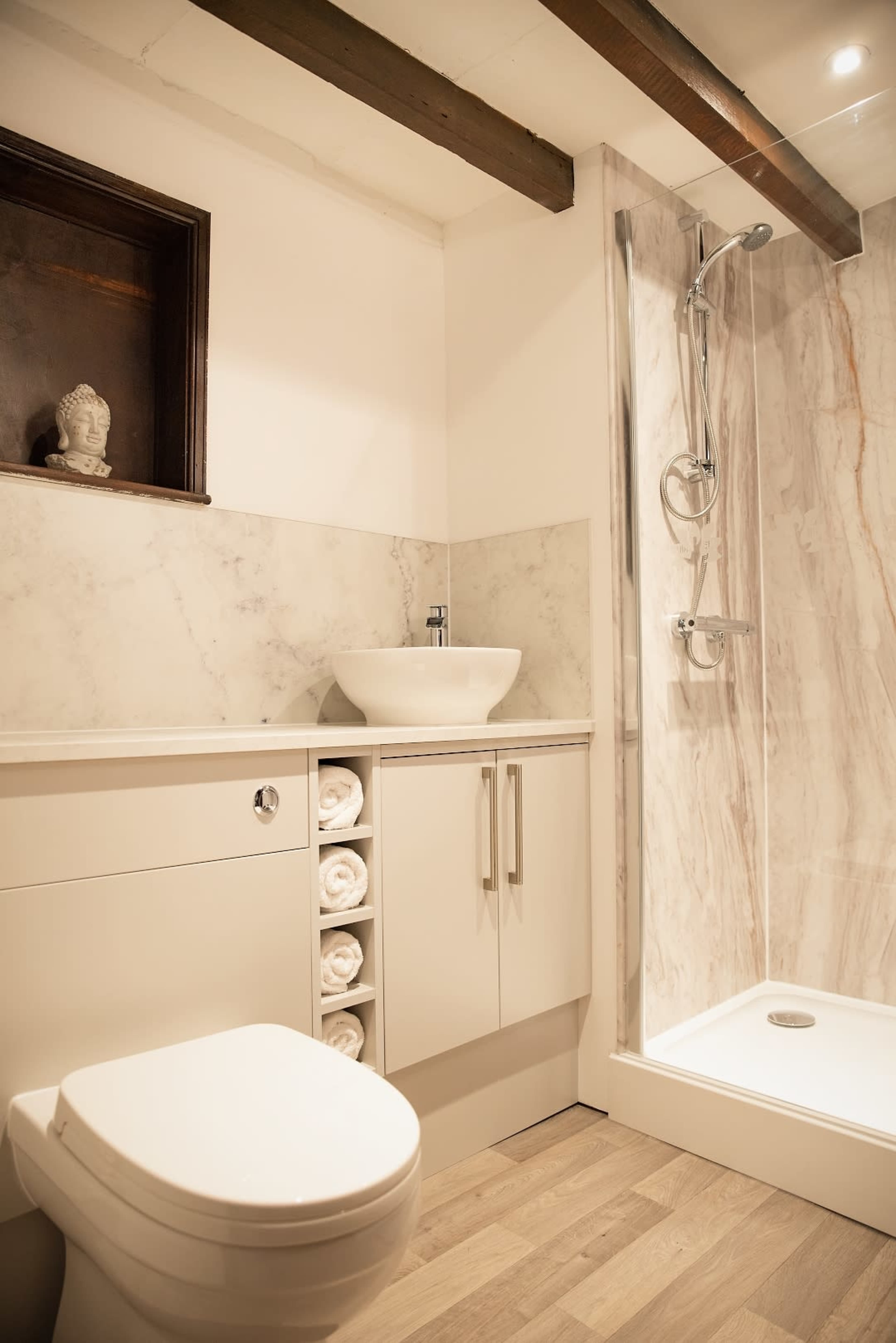 A modern bathroom featuring a shower, a sink with a wall-mounted faucet, a cabinet with neatly rolled towels, and a toilet.