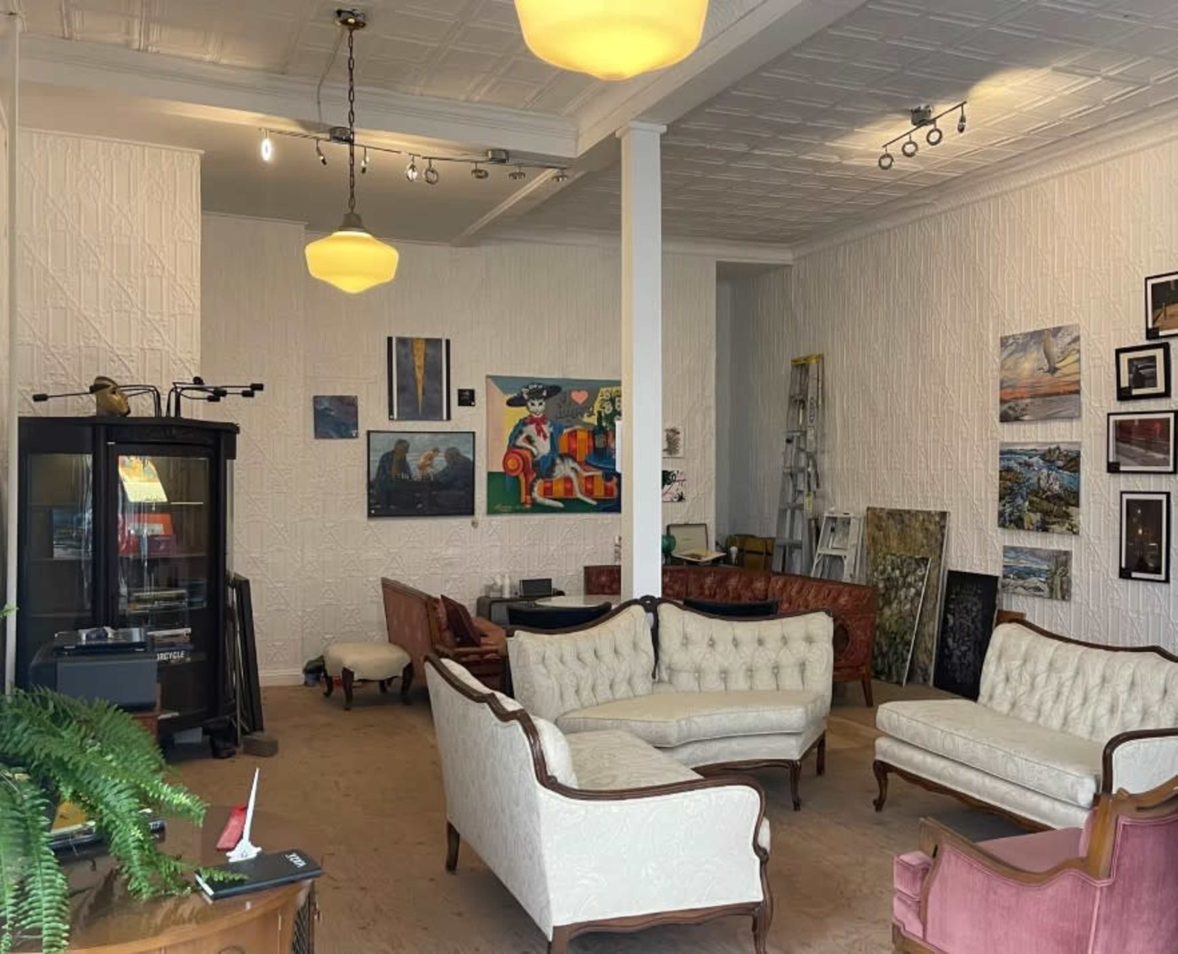 The image shows an art gallery with various seating options, wall-mounted artworks, and a few pieces of furniture scattered throughout the space.