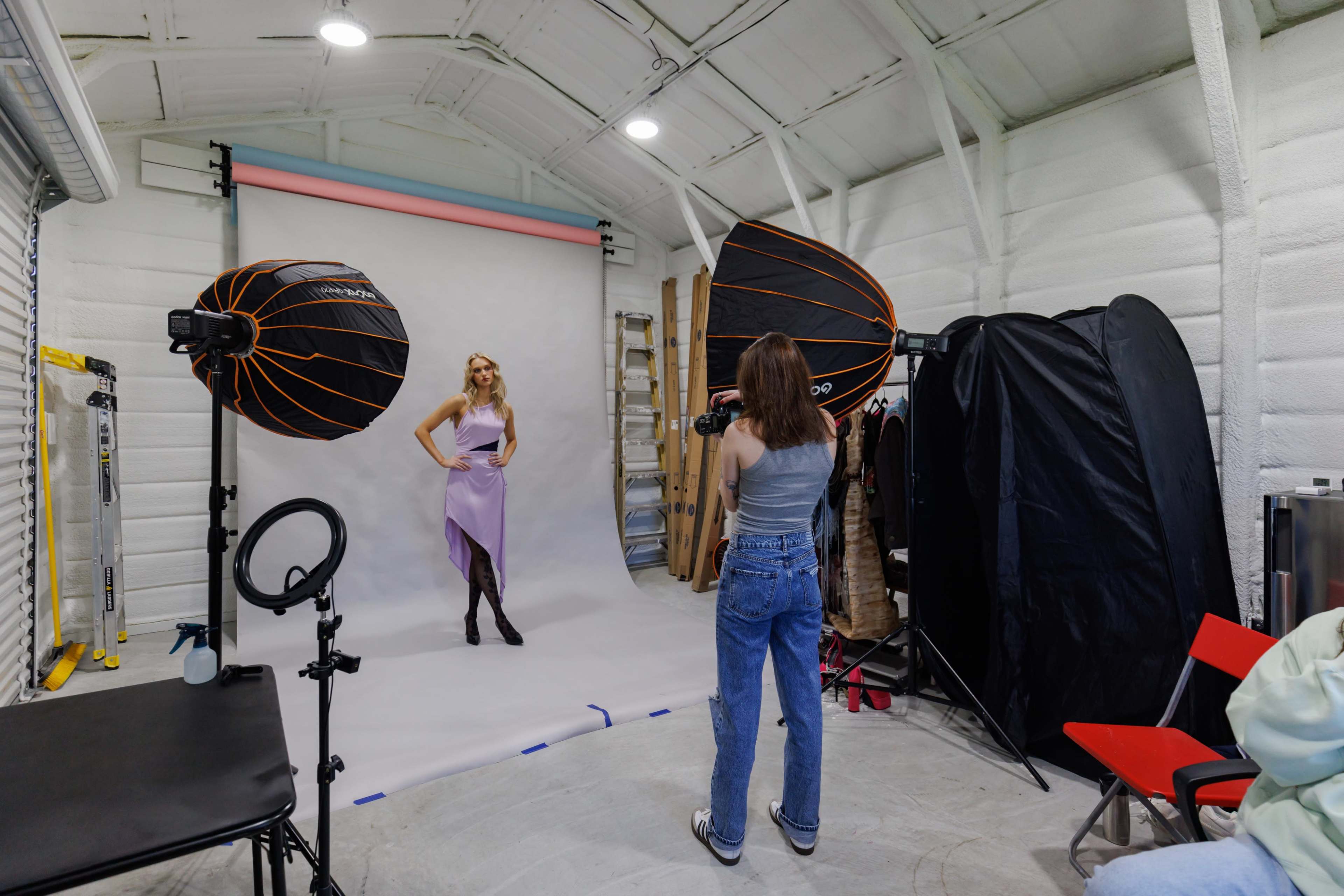 A photographer captures a model posing in front of a backdrop in a studio equipped with softbox lights.