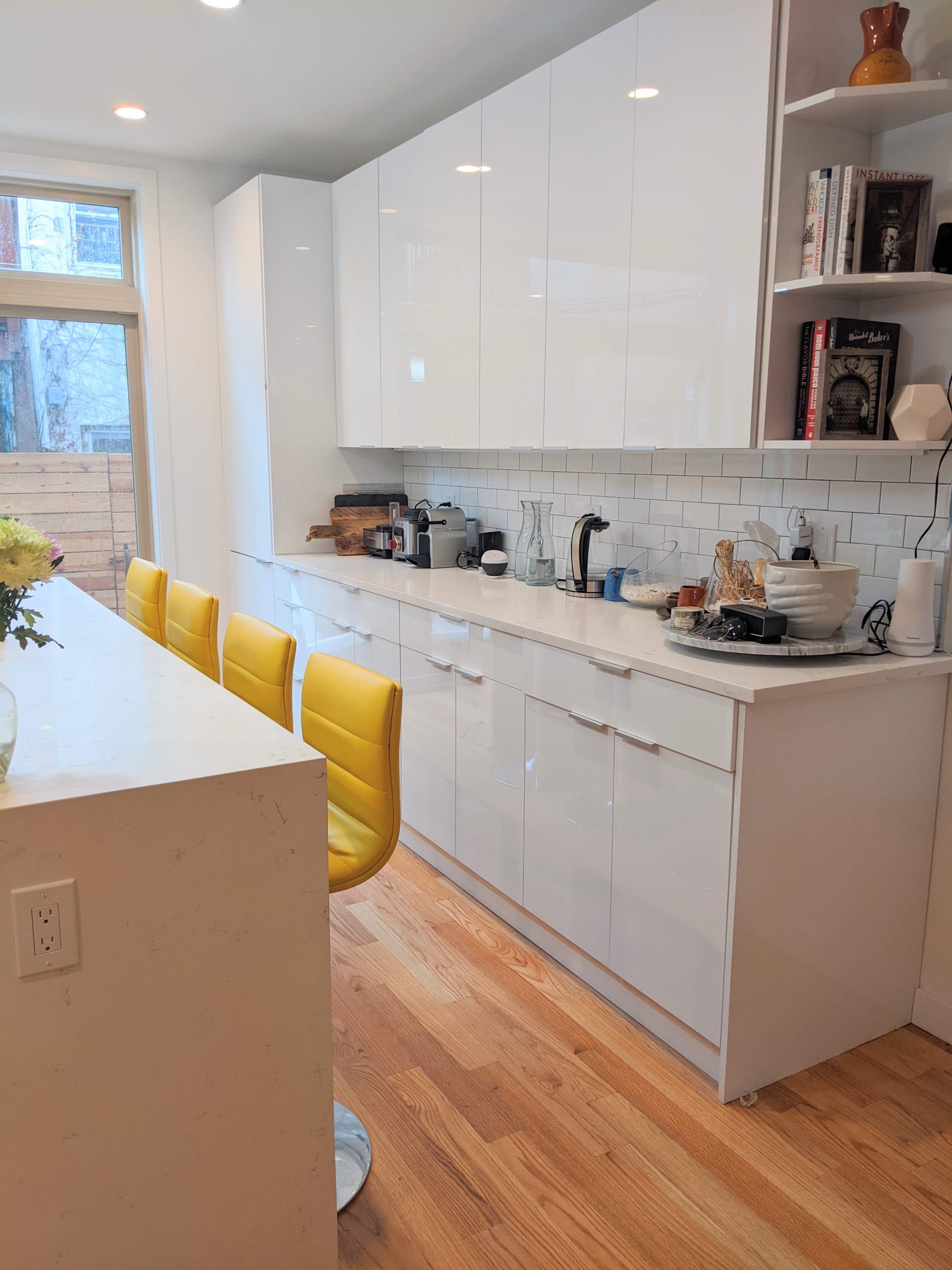 A modern kitchen with white cabinetry, a light-colored countertop, and four yellow bar stools at a large island.