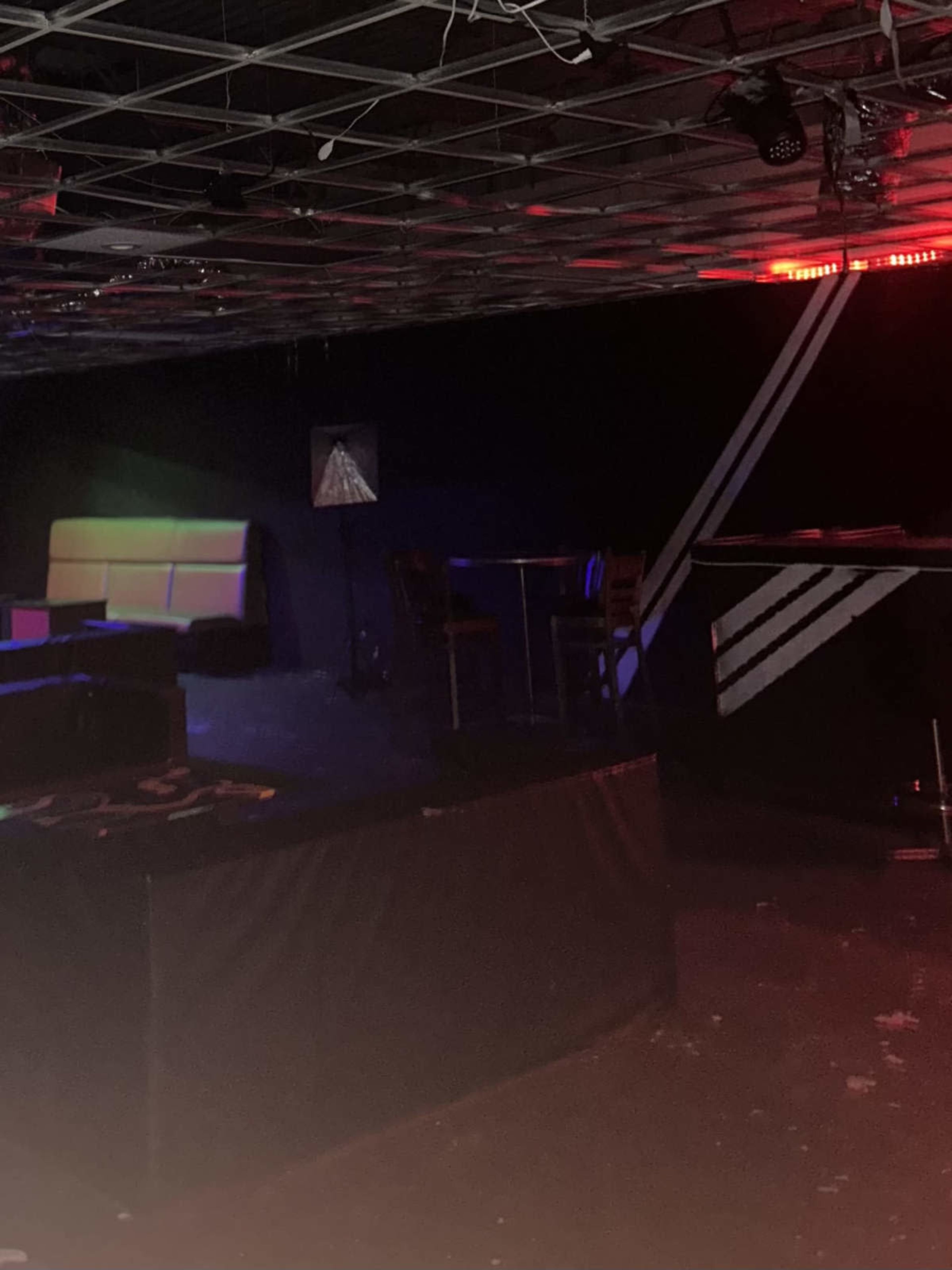 The image shows a dimly lit club interior with a seating area and a bar against a black backdrop.