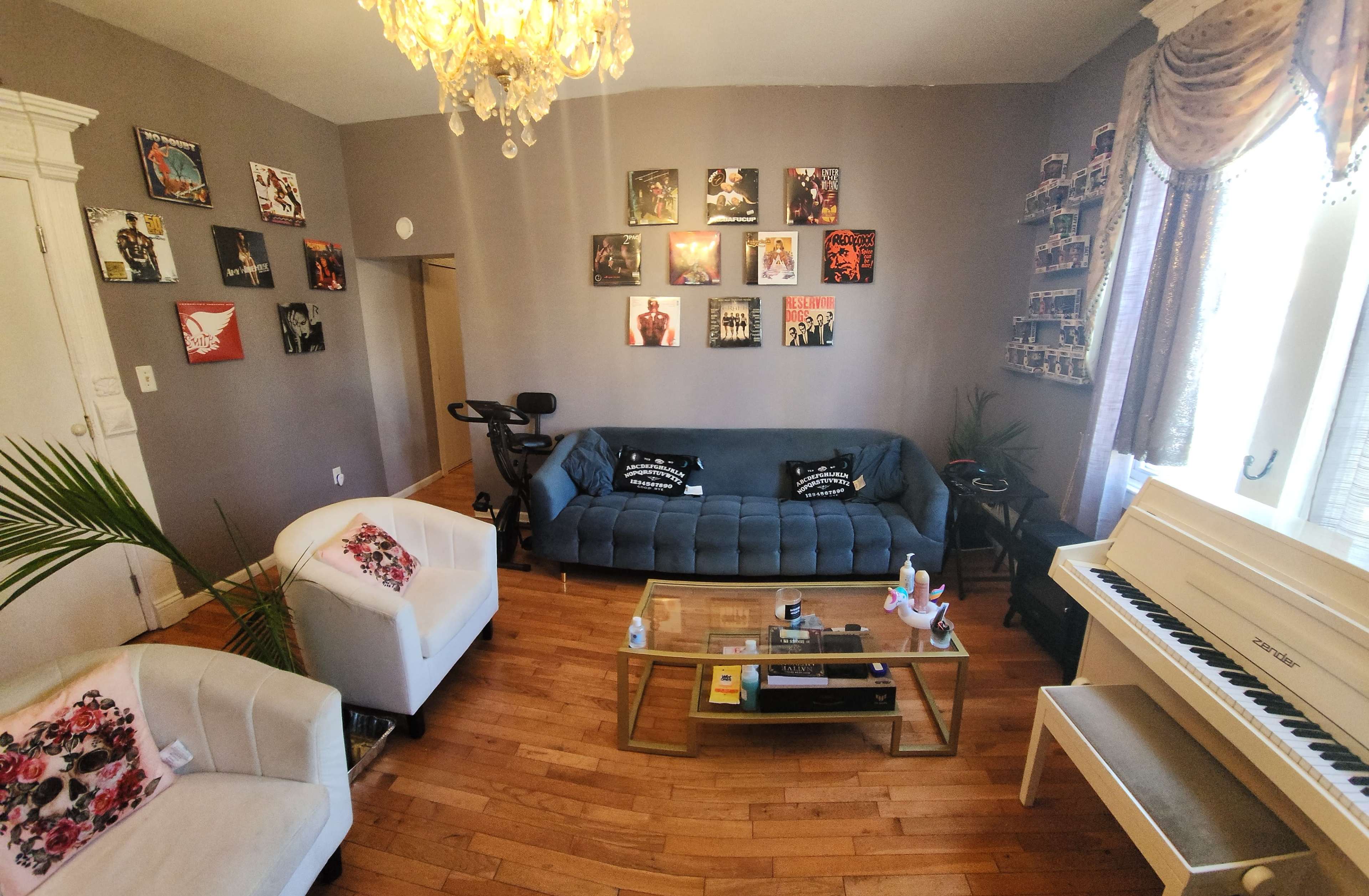 A living room with a blue couch, two white chairs, a coffee table, a piano, and various framed artworks on the walls.