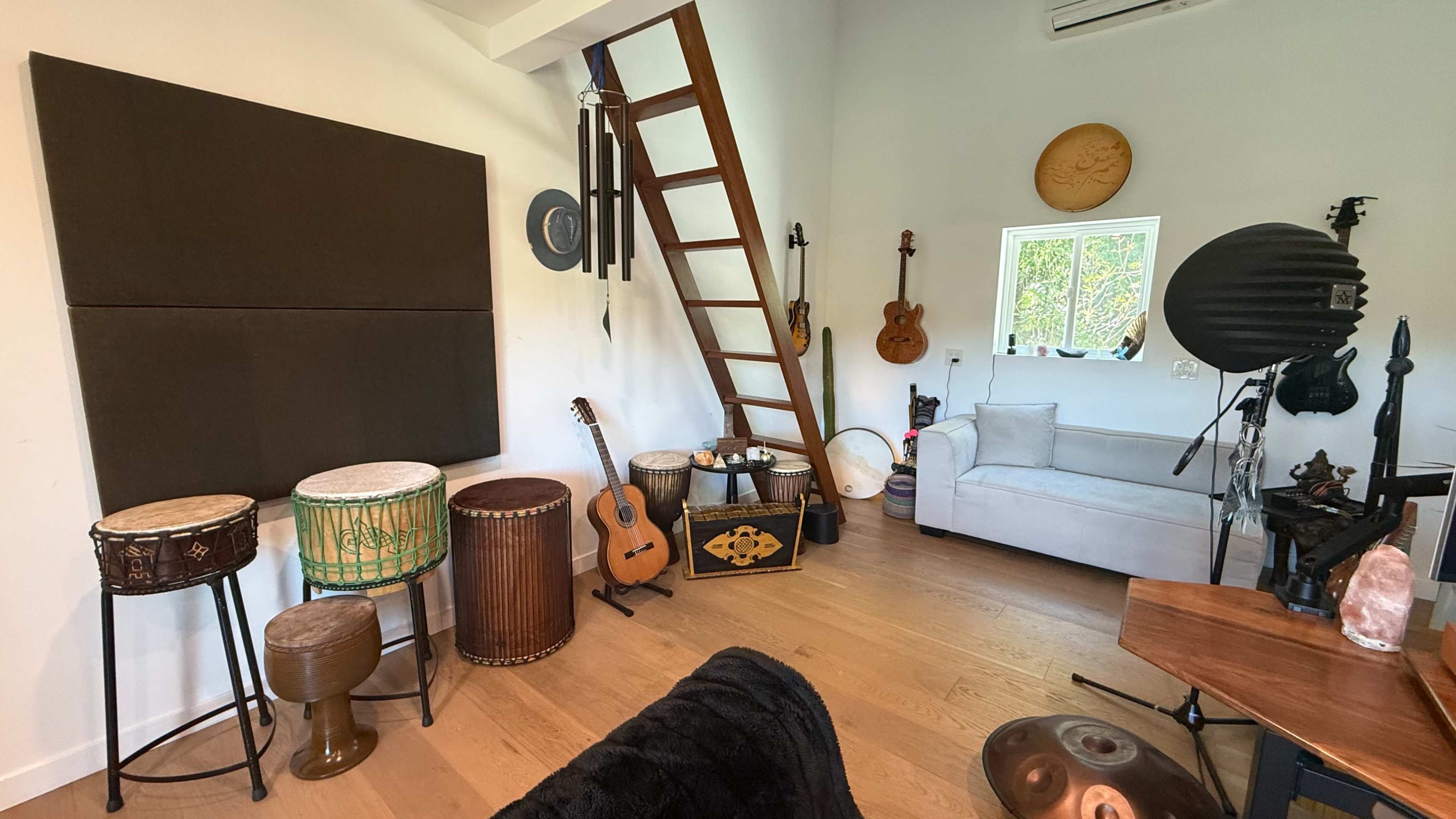 The image shows a cozy music room featuring various musical instruments, including drums, a guitar, and wind chimes, alongside a ladder leading to a loft area.
