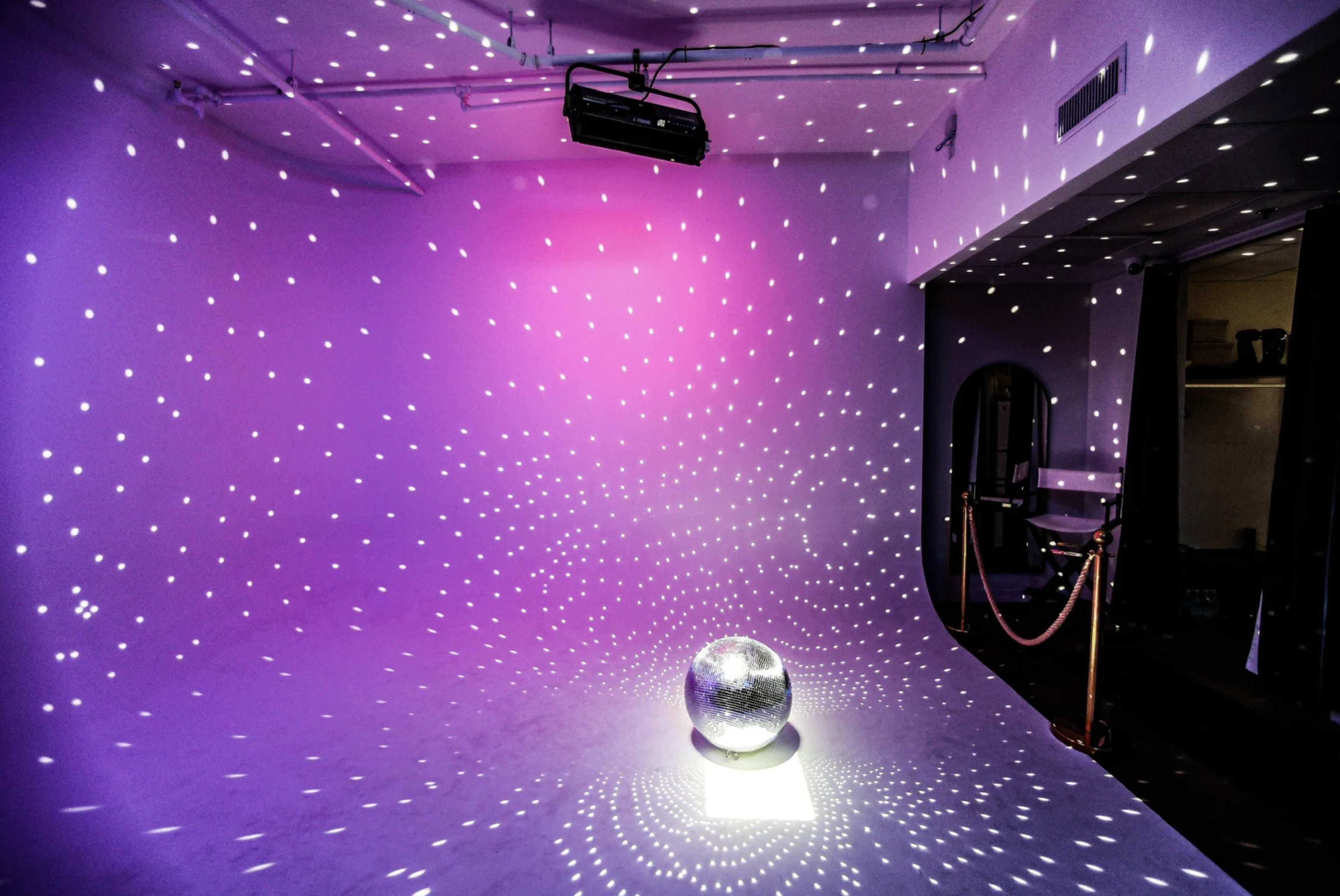 The scene features a shiny disco ball placed in a room, casting numerous light reflections on the walls and floor in purple hues.