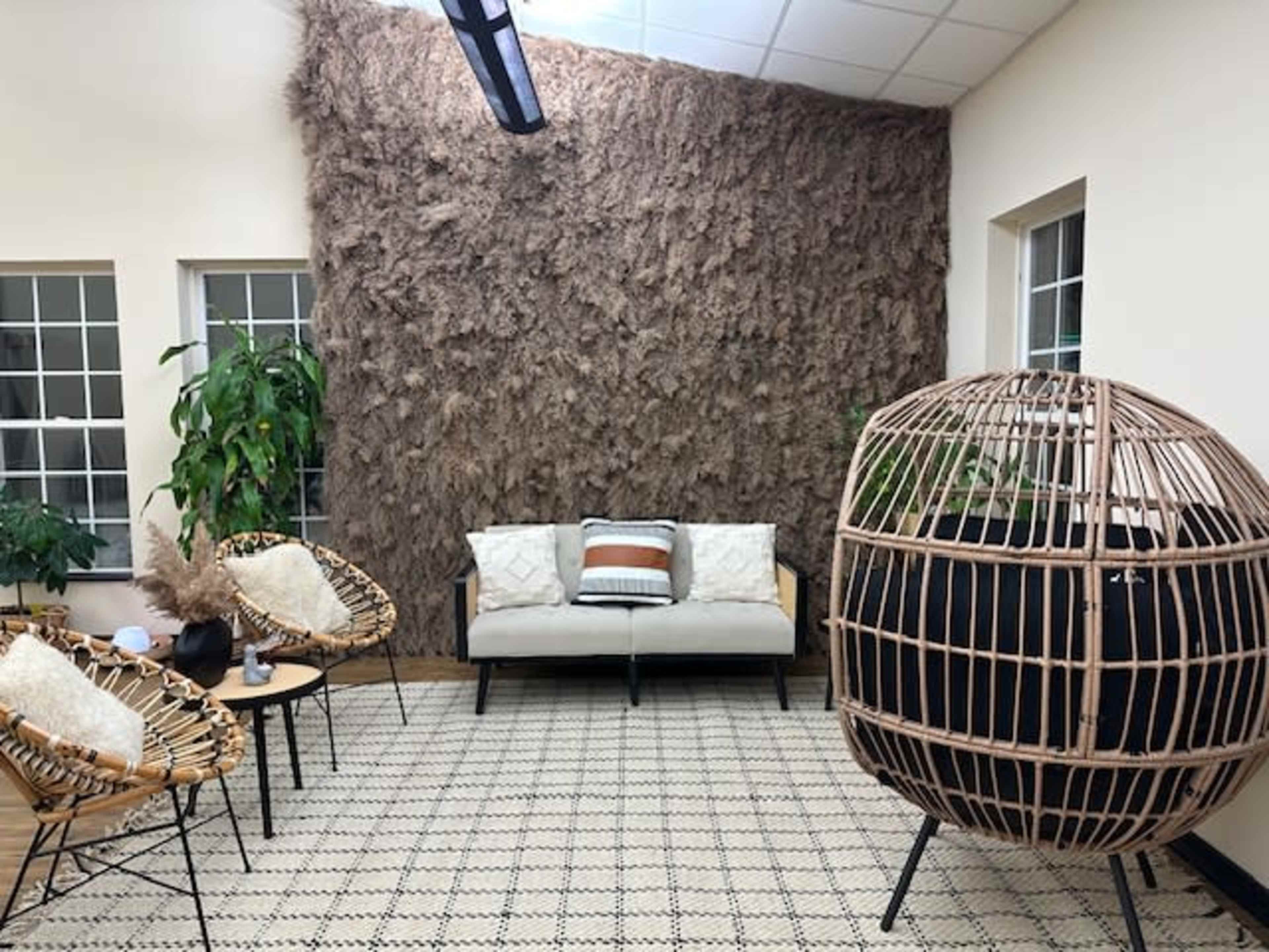 A cozy interior with a textured wall, a sofa, two woven chairs, and a large, round rattan structure beside indoor plants.