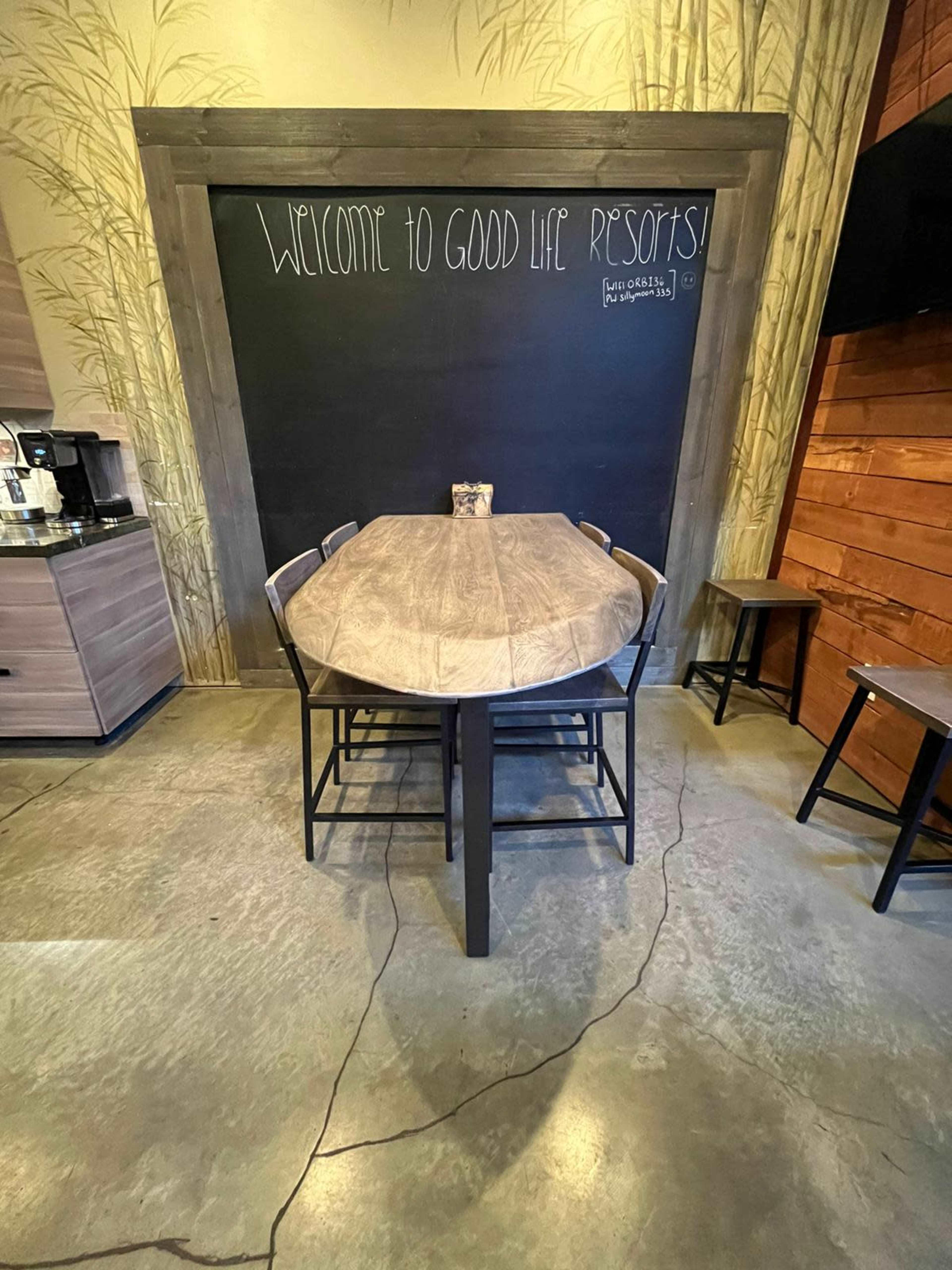 A wooden table surrounded by chairs in a cozy interior featuring a chalkboard with the text "Welcome to Good Life Resorts."