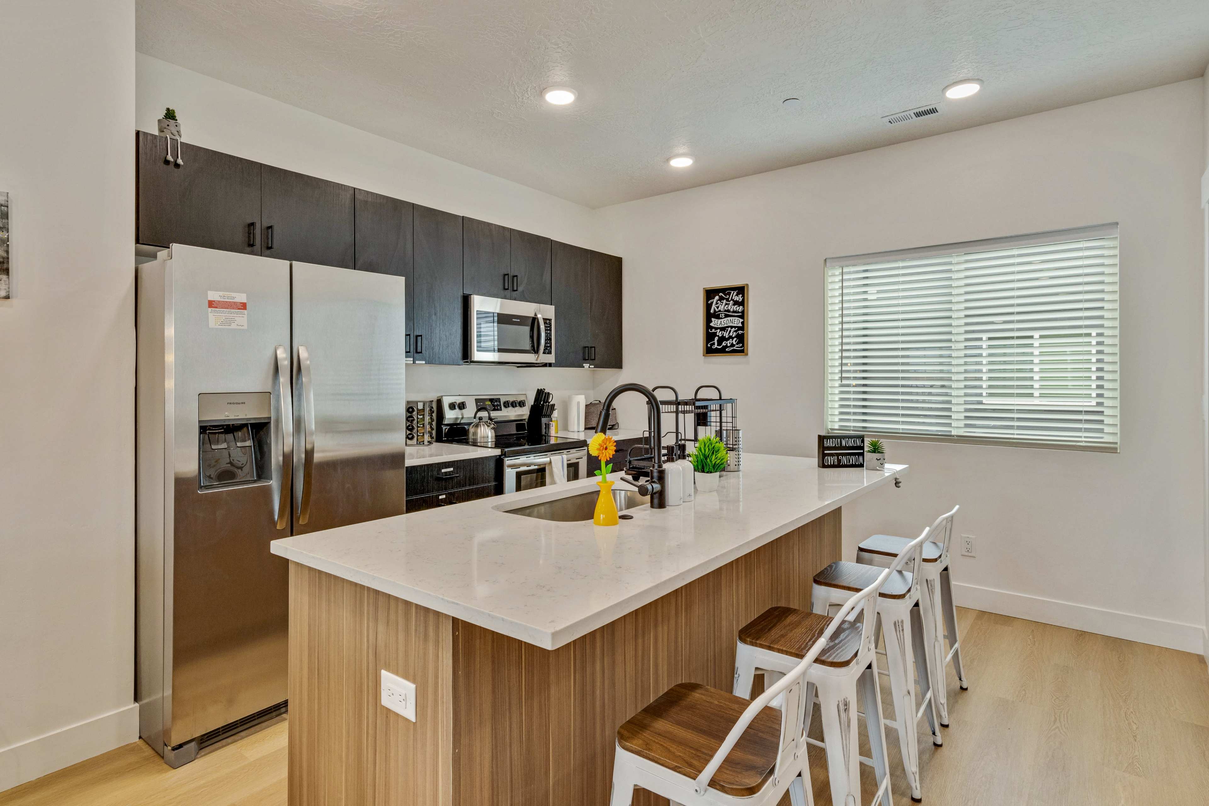 A modern kitchen features stainless steel appliances, a large island with bar stools, and sleek cabinetry.