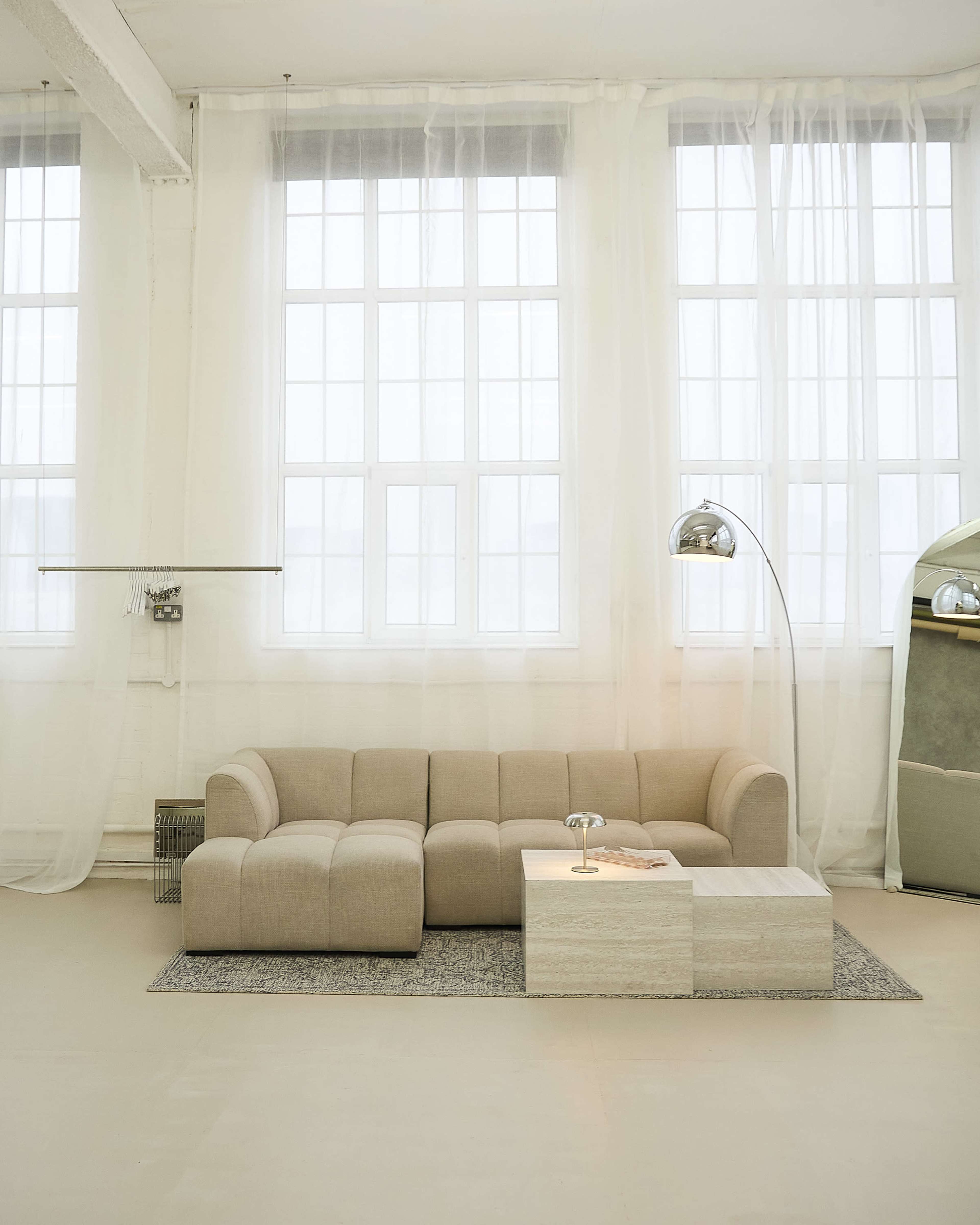 The image shows a modern, light-colored sofa with a matching coffee table set in a bright room with large windows and sheer curtains.