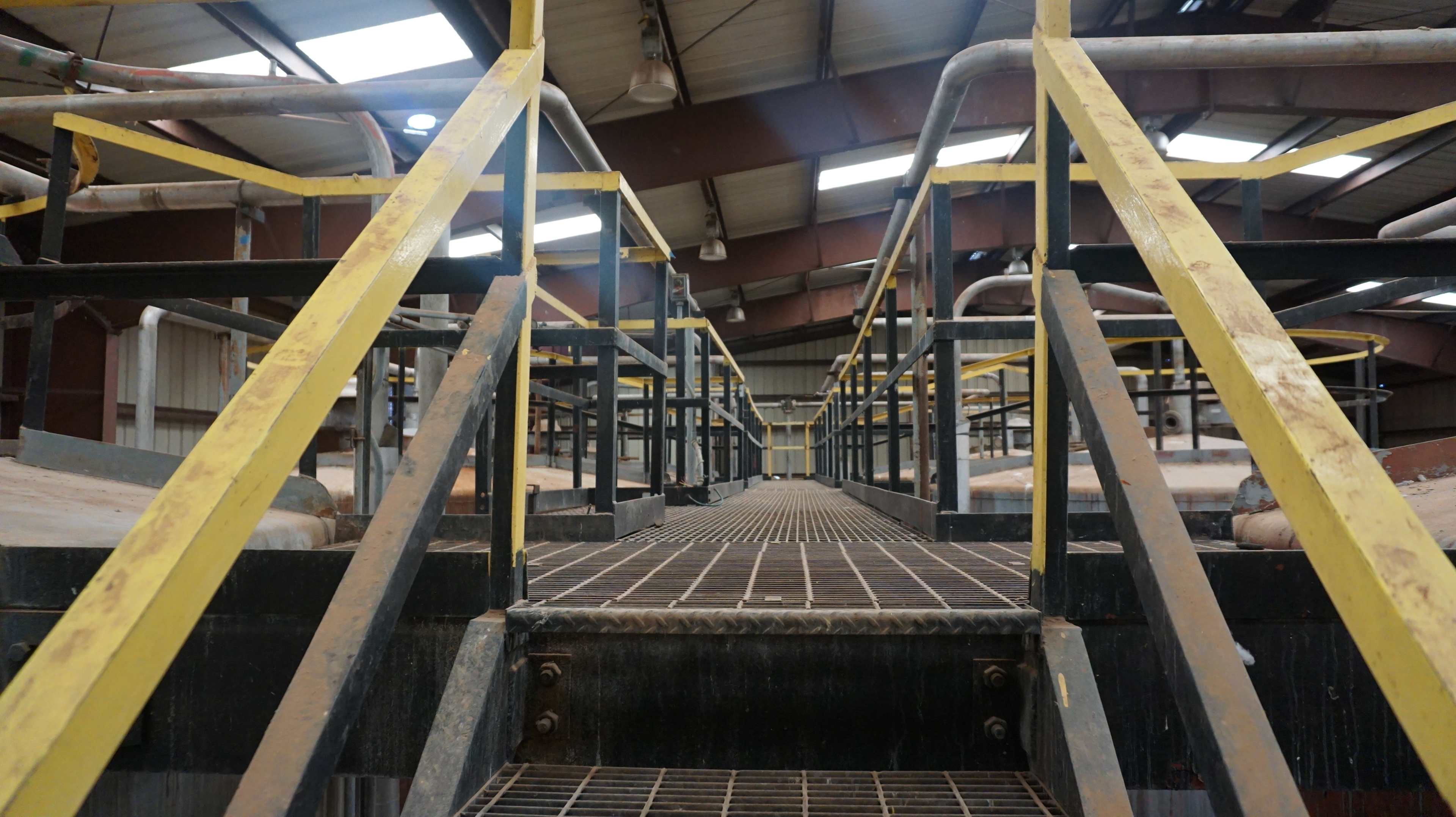 A view of a metal walkway with yellow railings leading through an industrial facility.