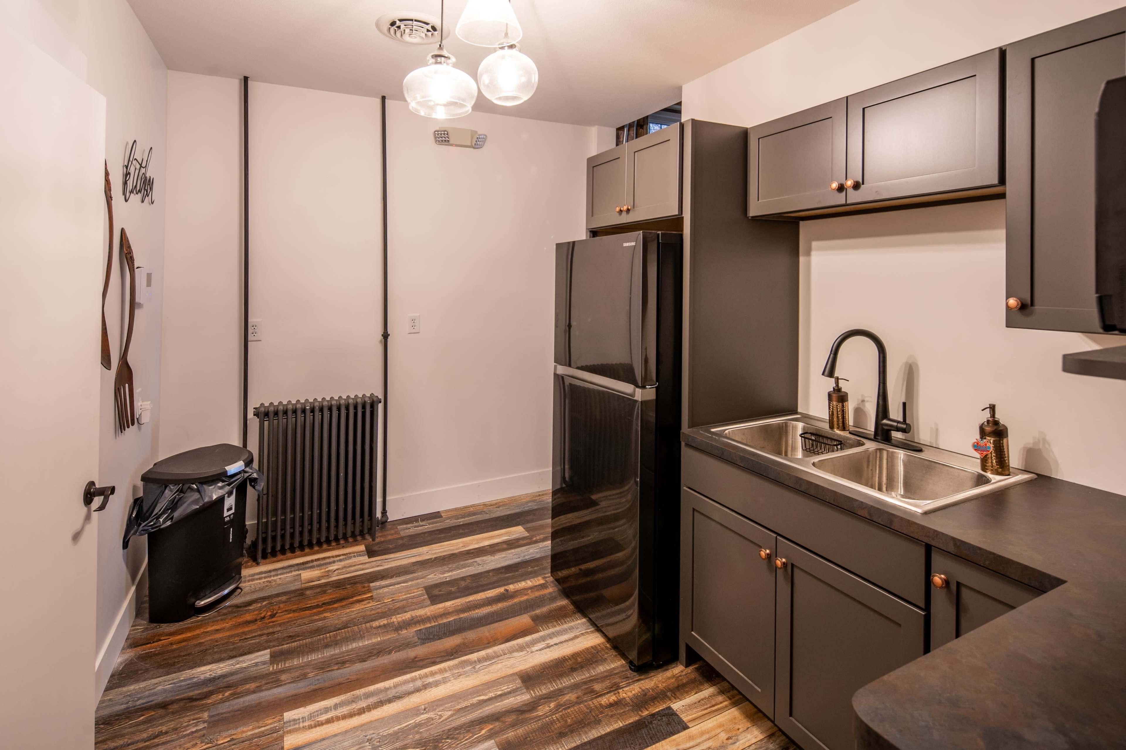 A modern kitchen features a black refrigerator, stainless steel sink, and dark cabinetry with hardwood floors.