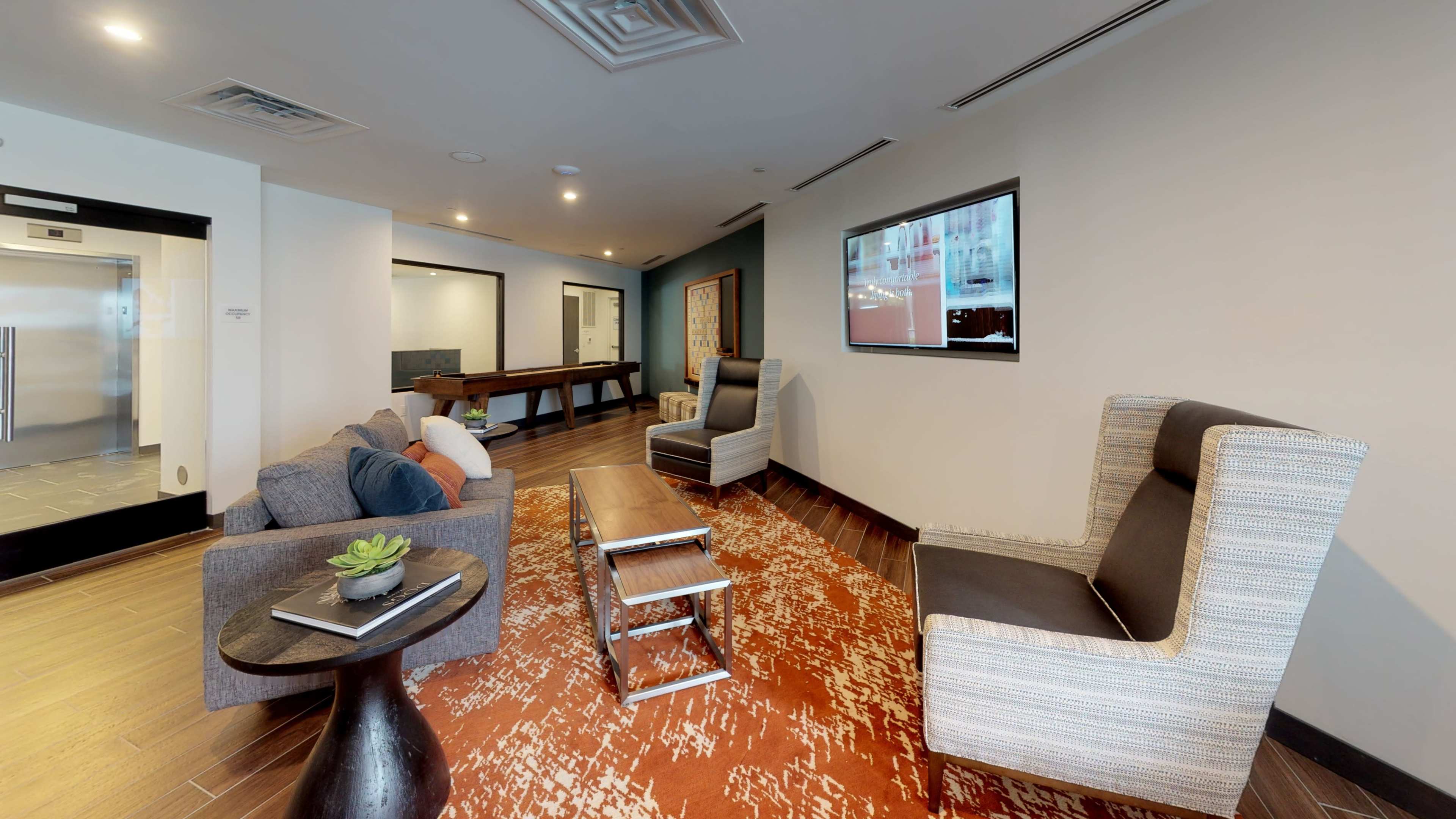 A modern lounge area with two armchairs, a coffee table, a sofa, and an elevator door visible in the background.