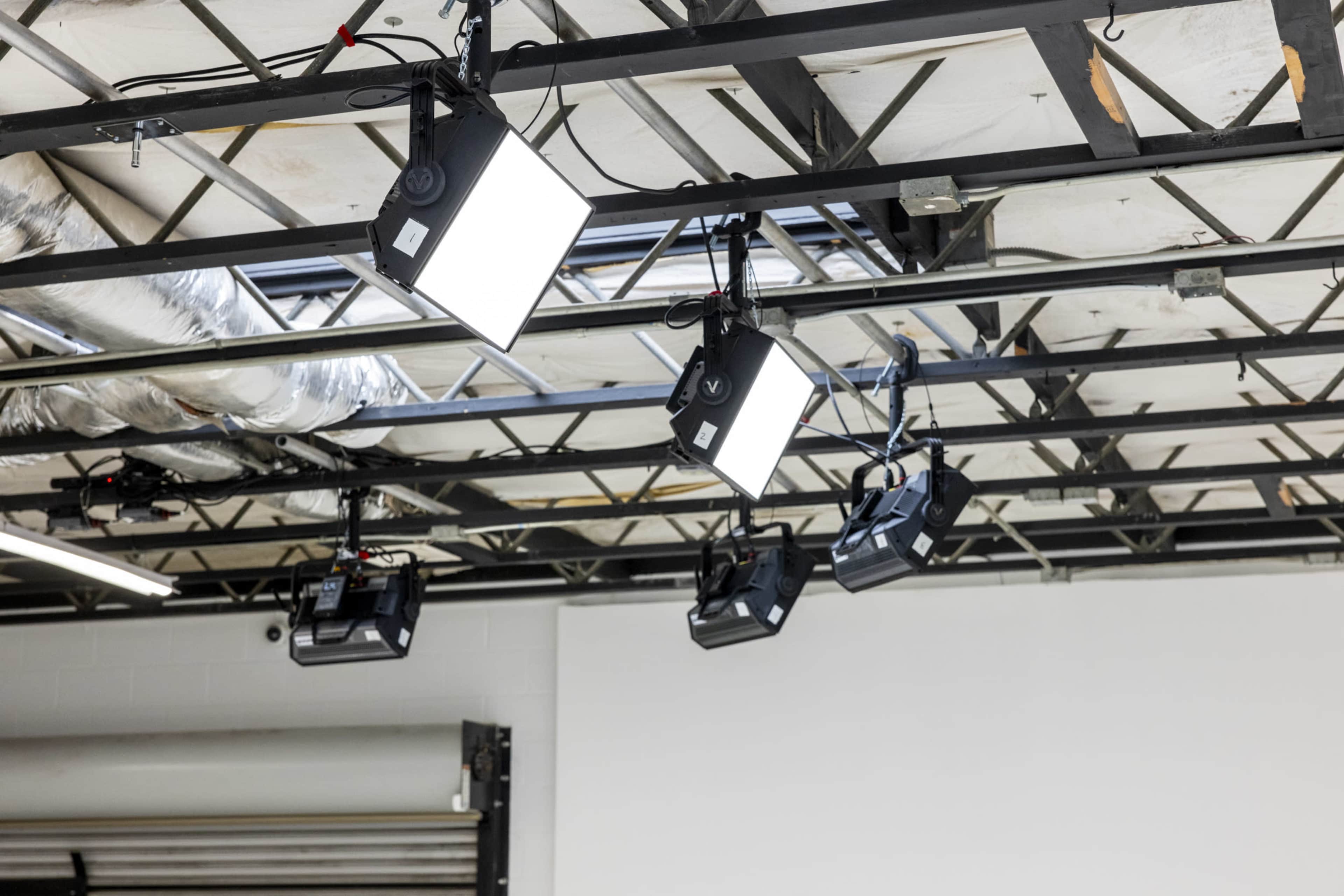 The image shows a ceiling with multiple light fixtures mounted, including square LED lights and several black studio lights.