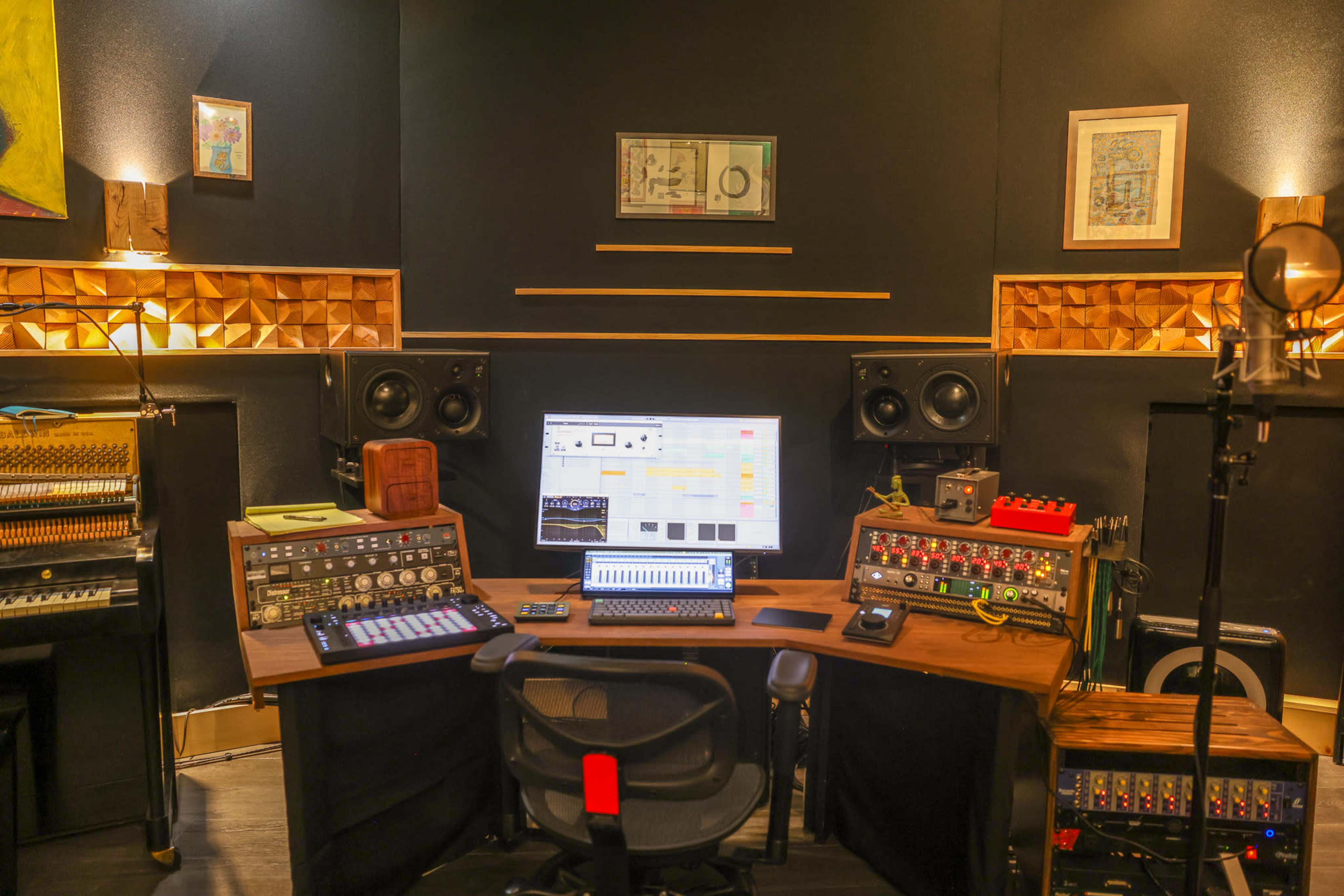 The image shows a well-equipped music production studio with a large digital audio workstation, various audio equipment, and a microphone set up for recording.