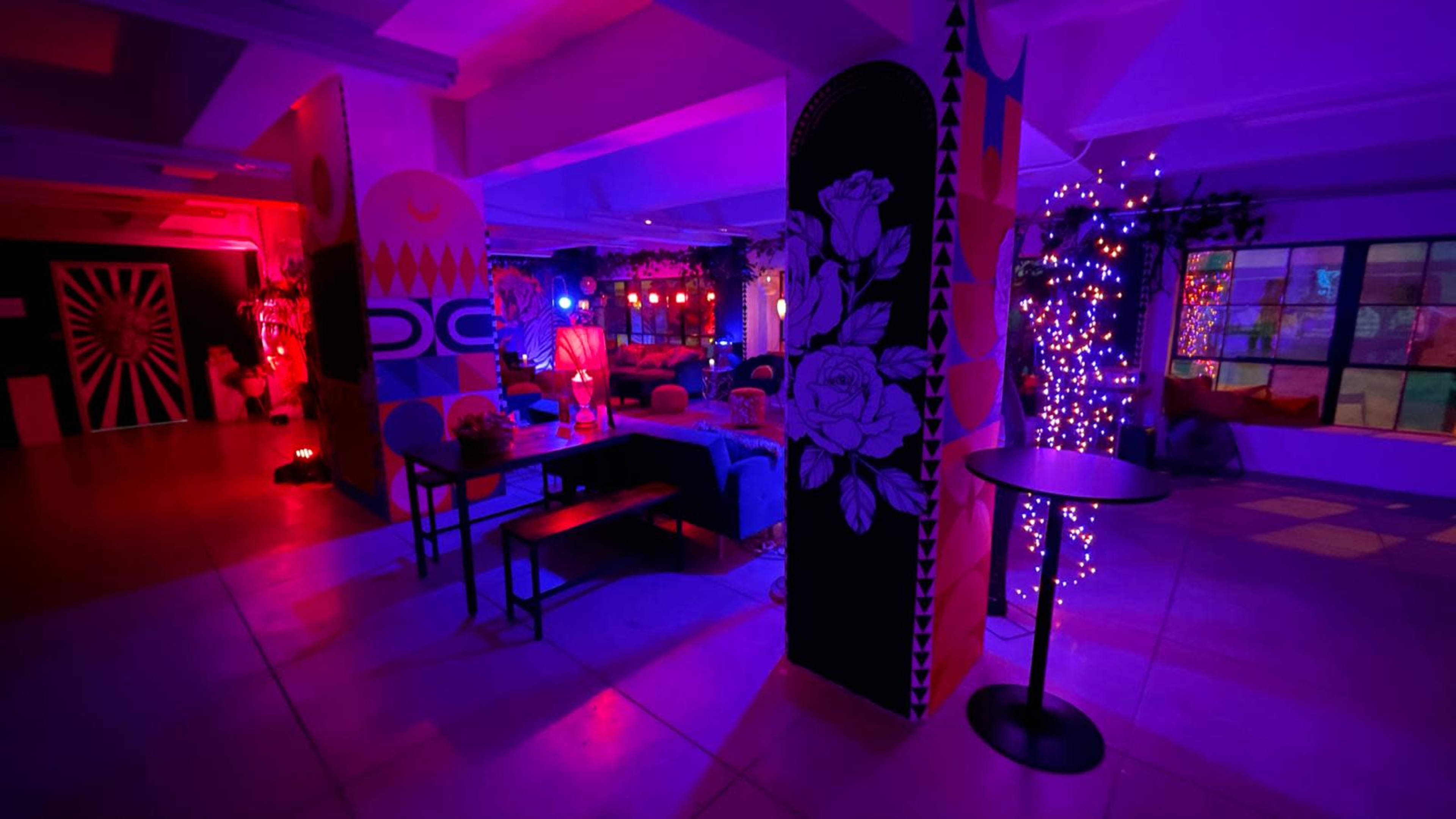 The image shows a vibrant, colorful interior space with illuminated decorations, seating areas, and artistic wall designs.