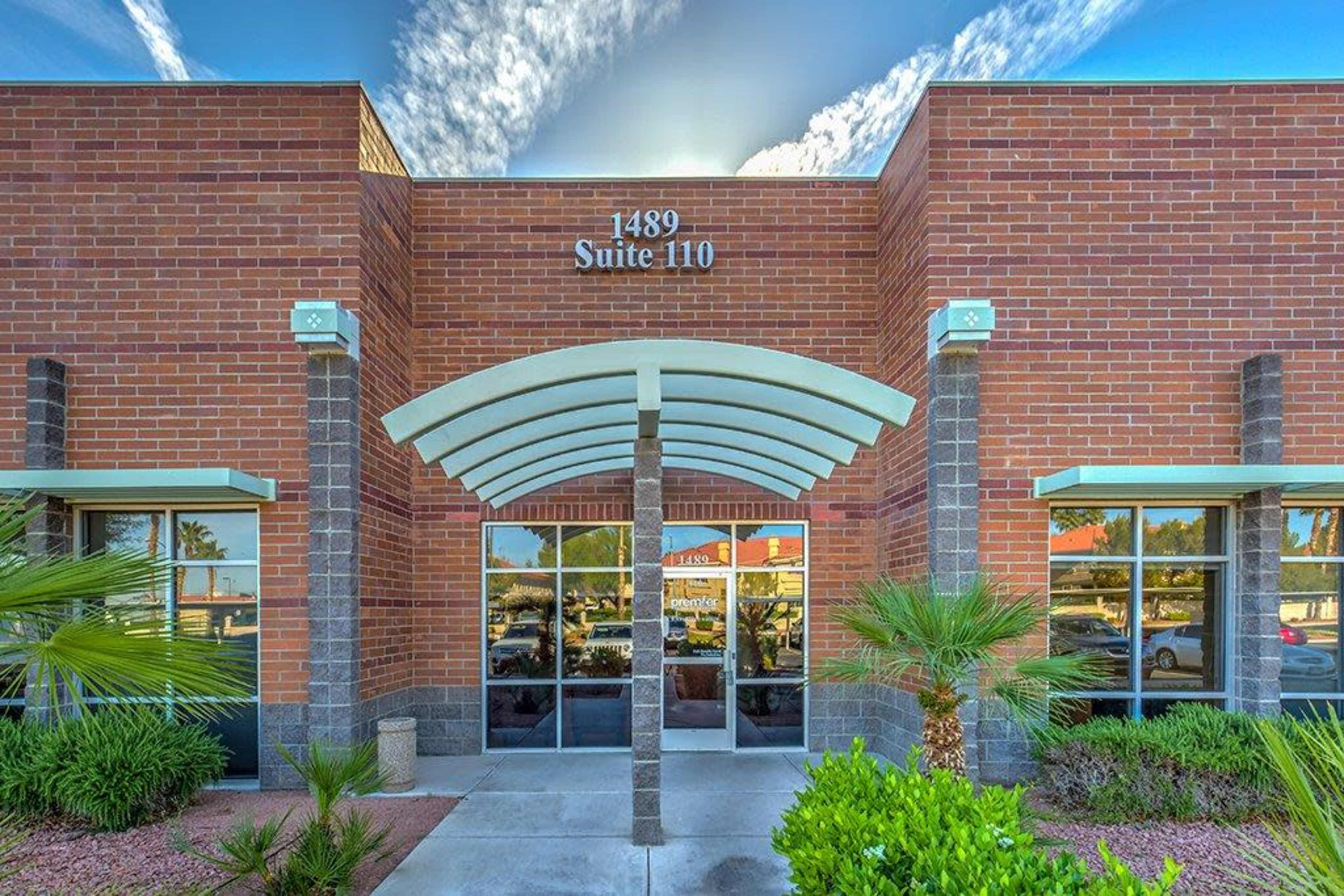 The image shows a brick commercial building with a covered entrance and palm trees in front, displaying the address "1489 Suite 110."
