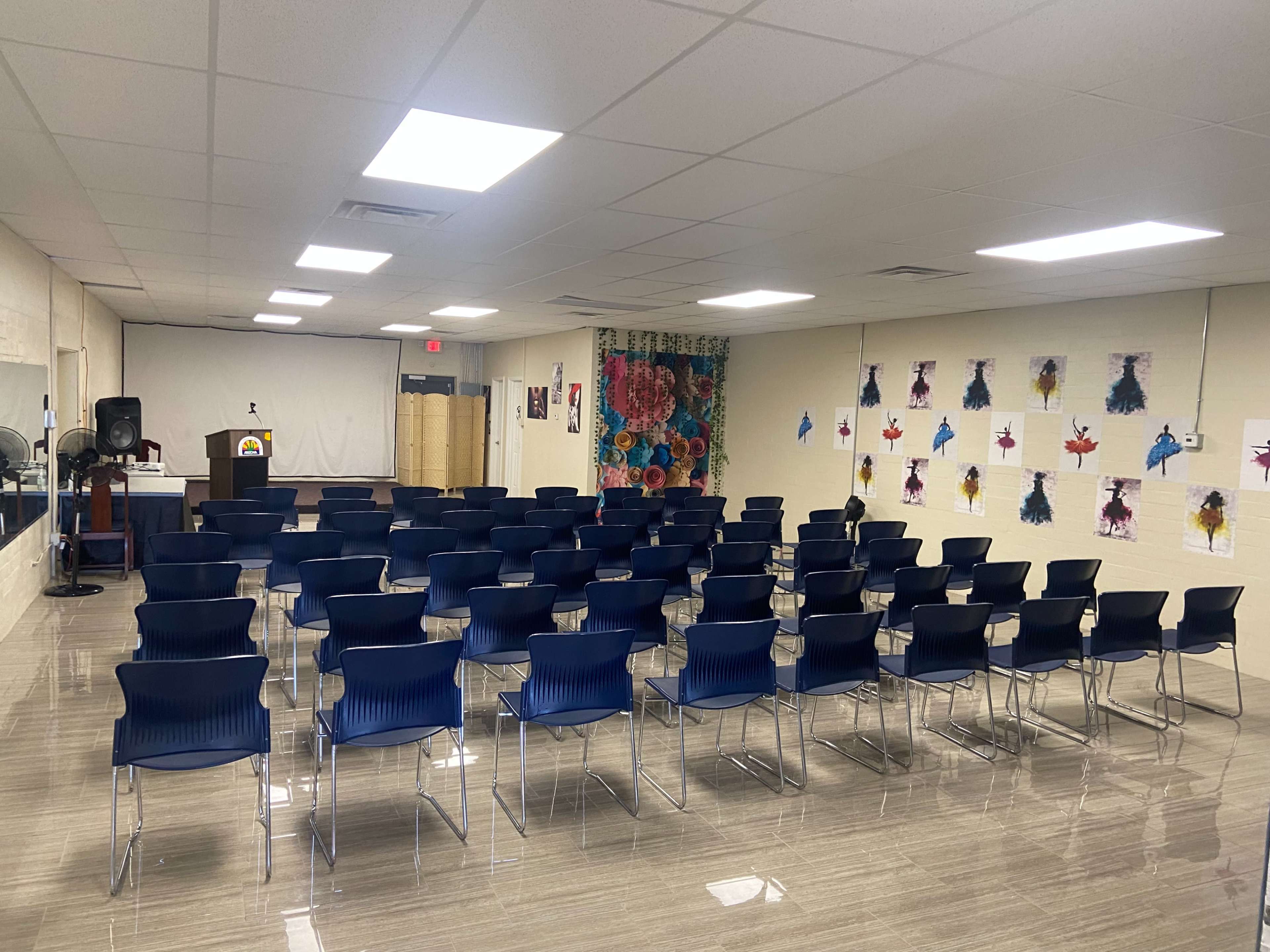 A spacious, empty meeting room arranged with rows of blue chairs facing a presentation area at the front.