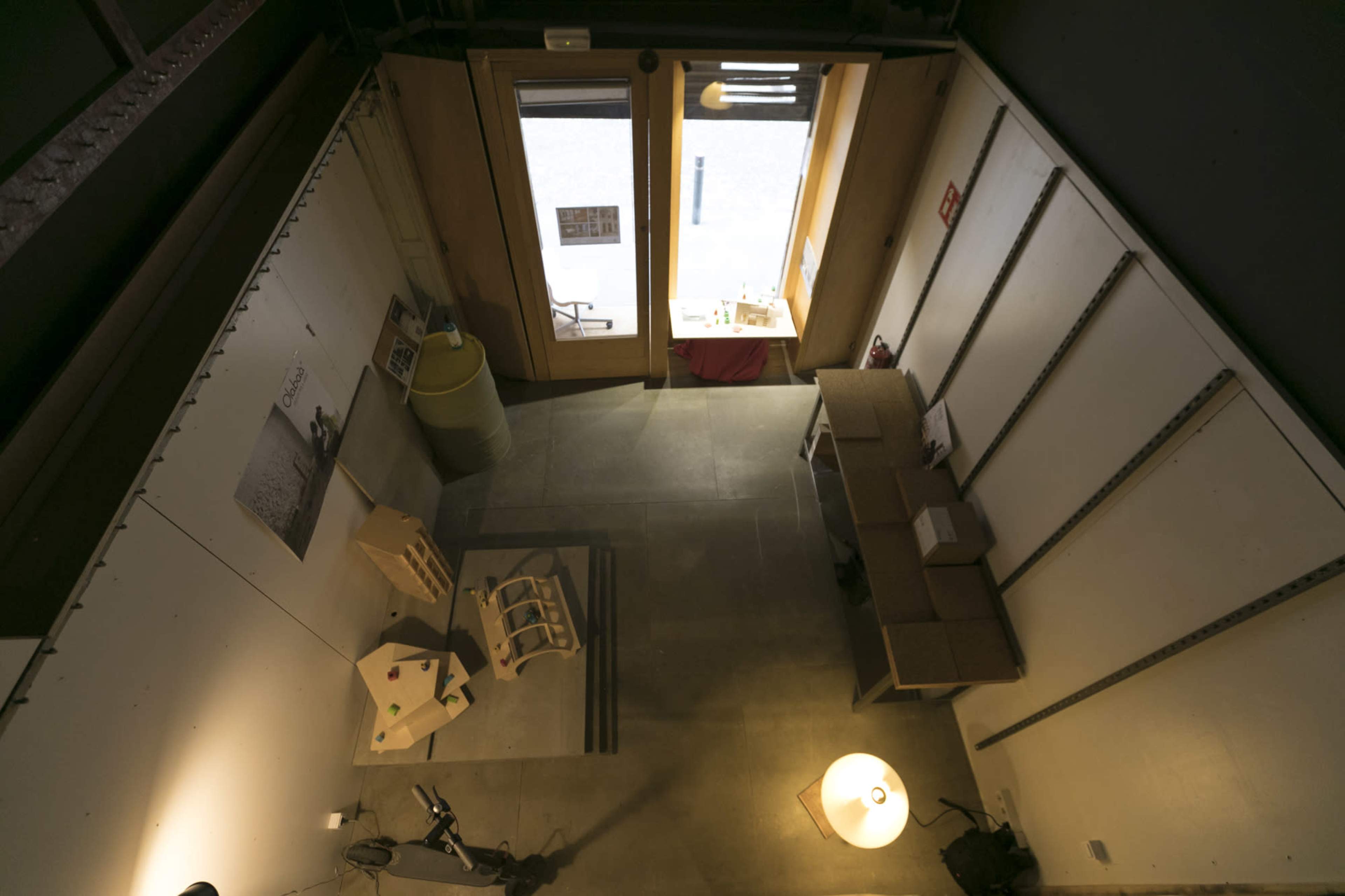 An overhead view of a minimalistic indoor space with wooden doors, concrete flooring, and a few scattered furniture pieces, including a table and several display items.