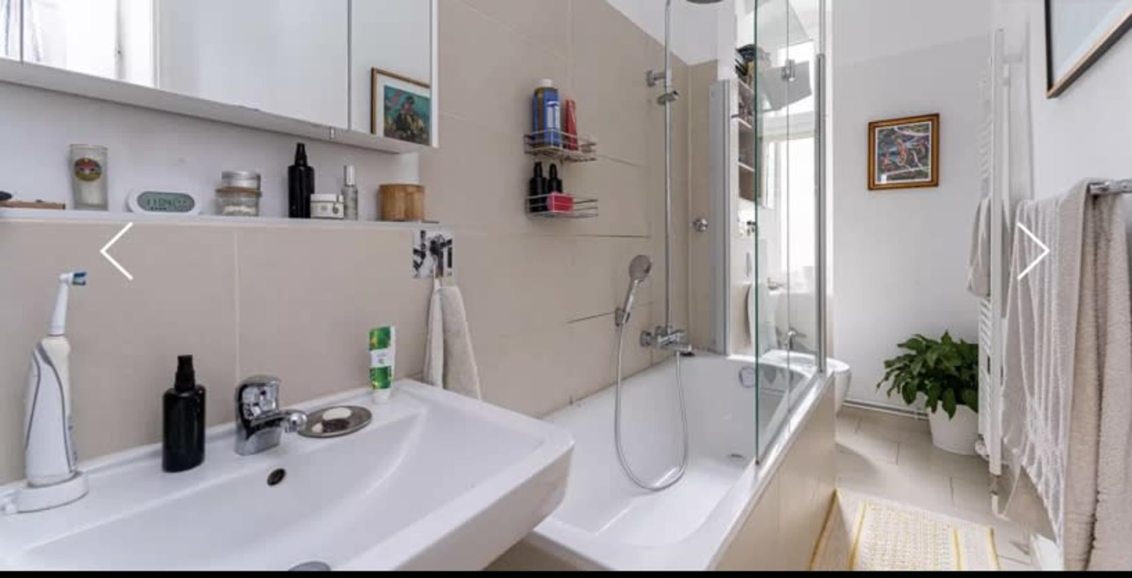 A modern bathroom featuring a bathtub with a glass shower enclosure, a sink with toiletries, and a towel rack.