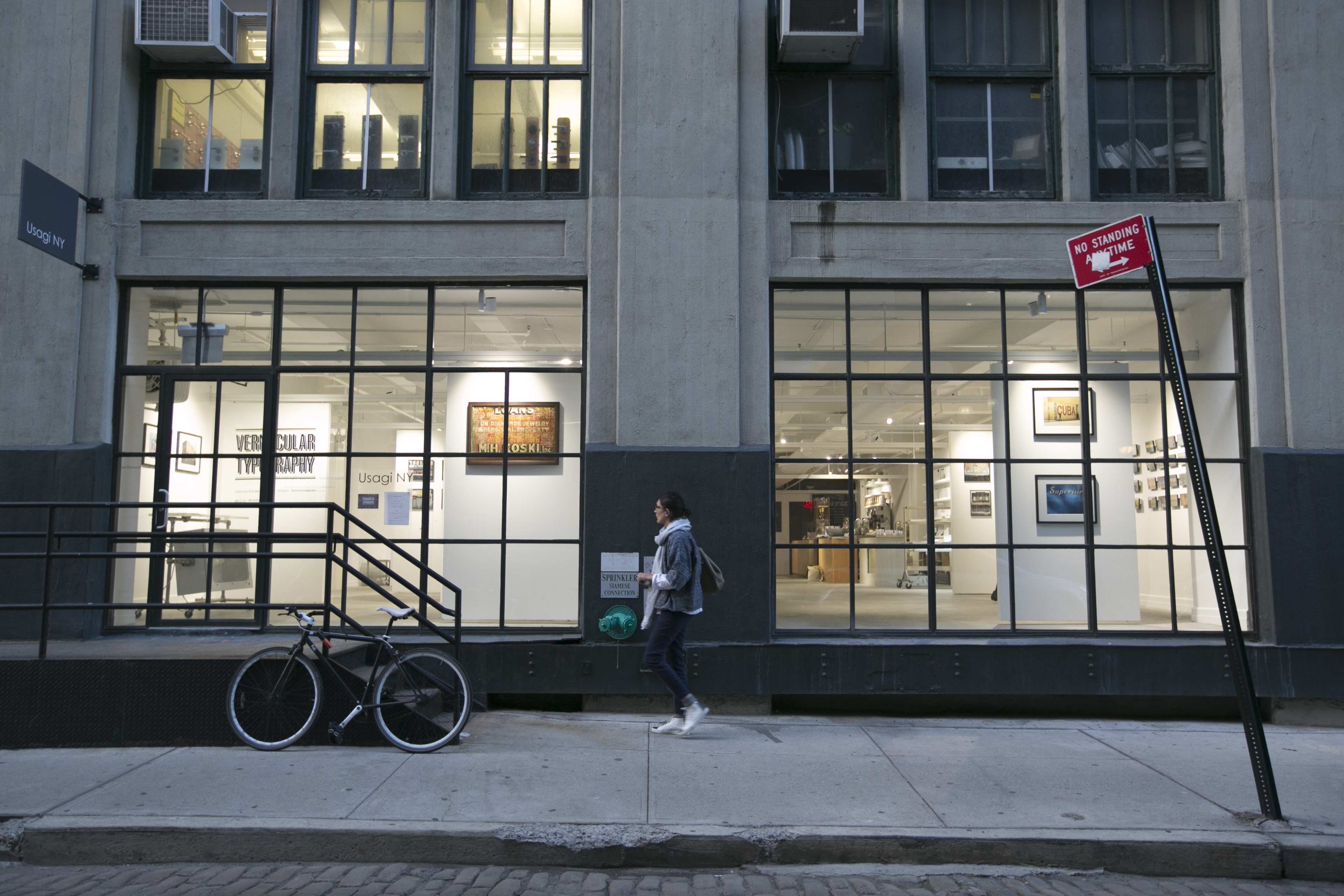 A person walks along the sidewalk next to a gallery with large windows and a bicycle parked nearby.
