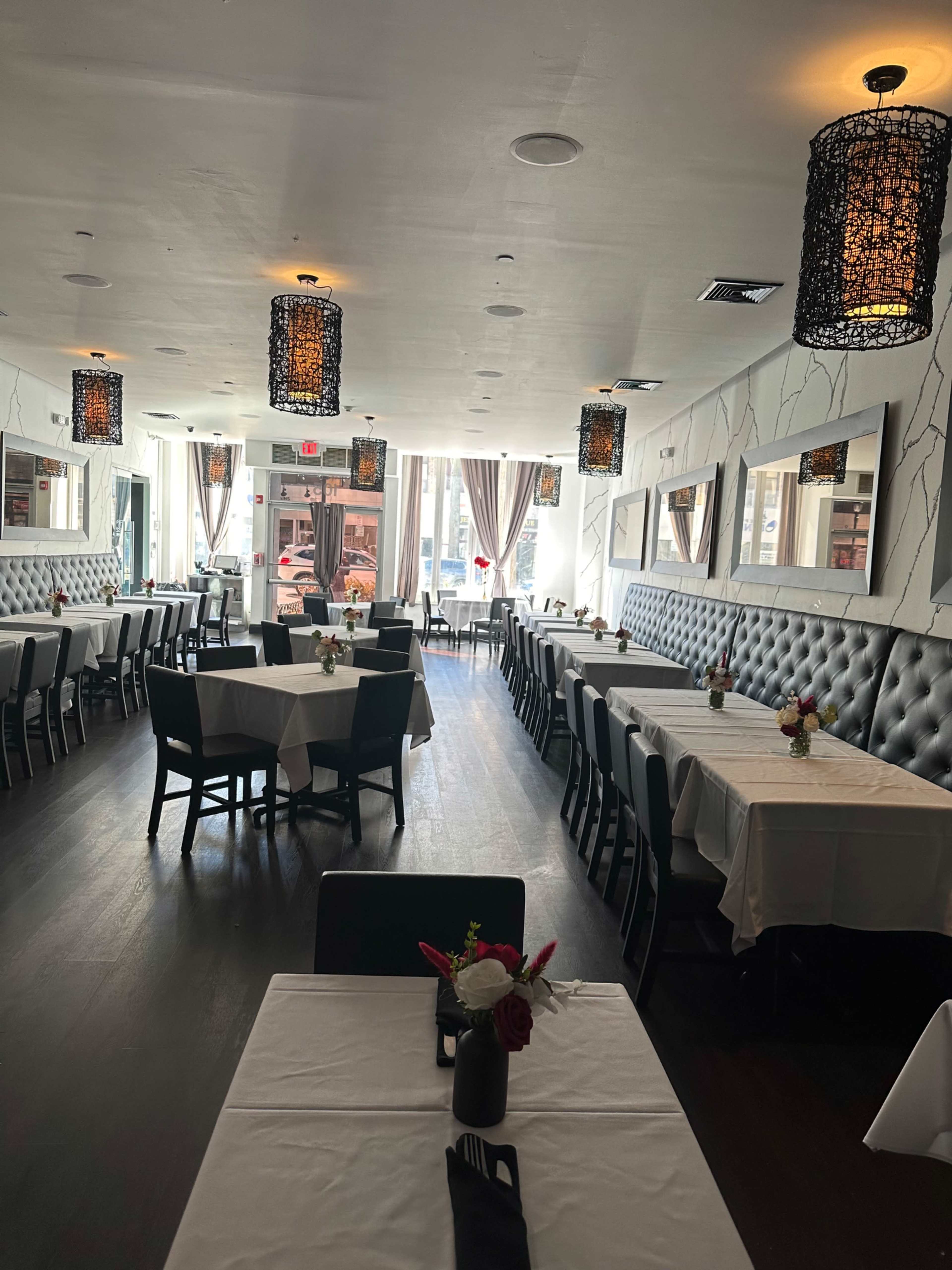The image shows a spacious restaurant dining area with neatly arranged tables, white tablecloths, and decorative lighting fixtures.
