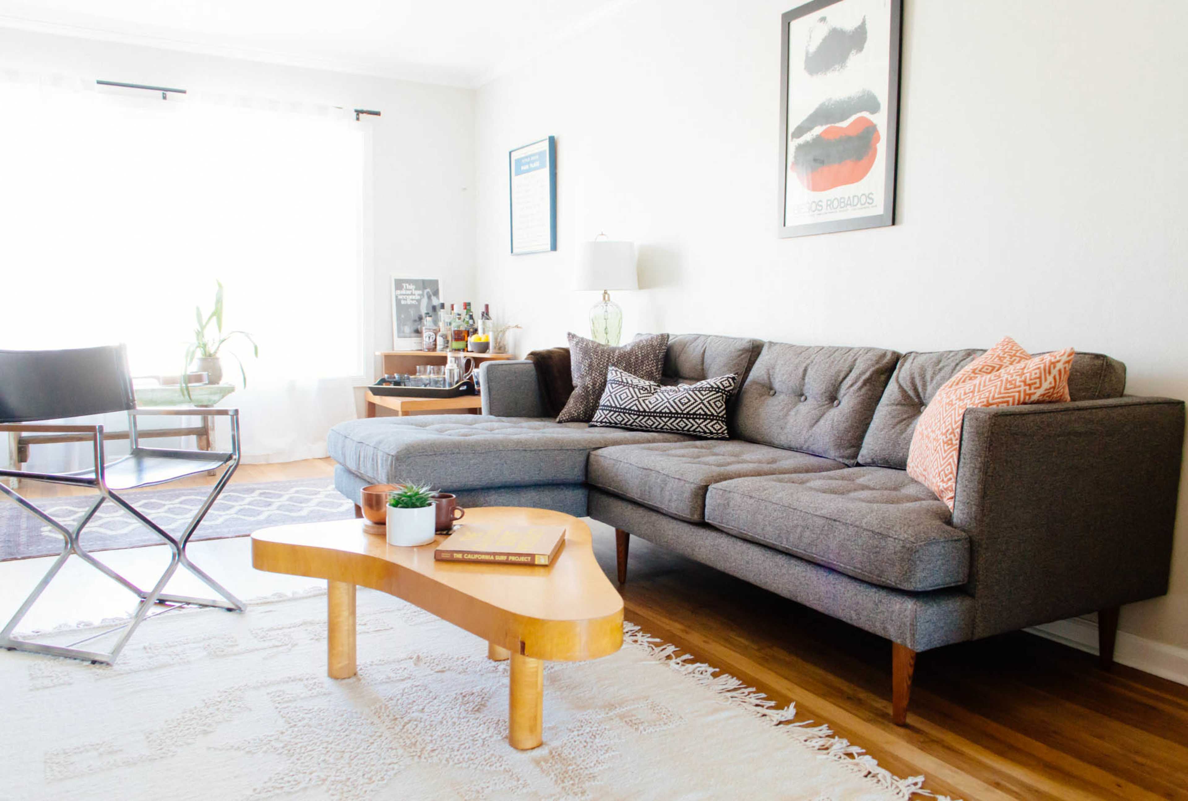 A modern living room with a gray sectional sofa, a wooden coffee table, and a glass dining chair, complemented by wall art and a plant in the background.