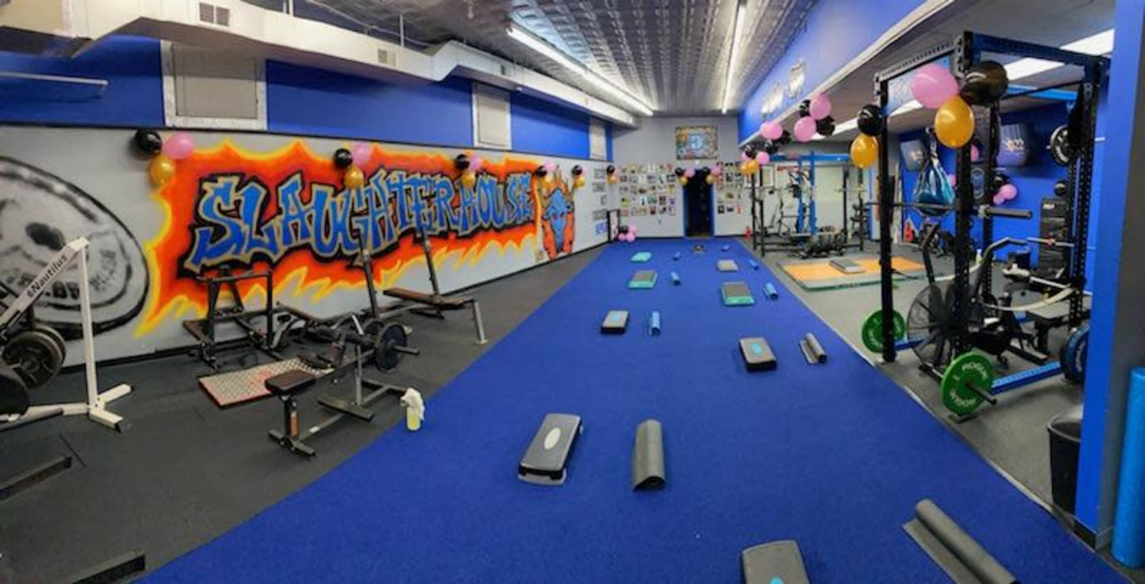 A gym interior with workout equipment, exercise mats, and colorful balloons on the walls and ceiling.