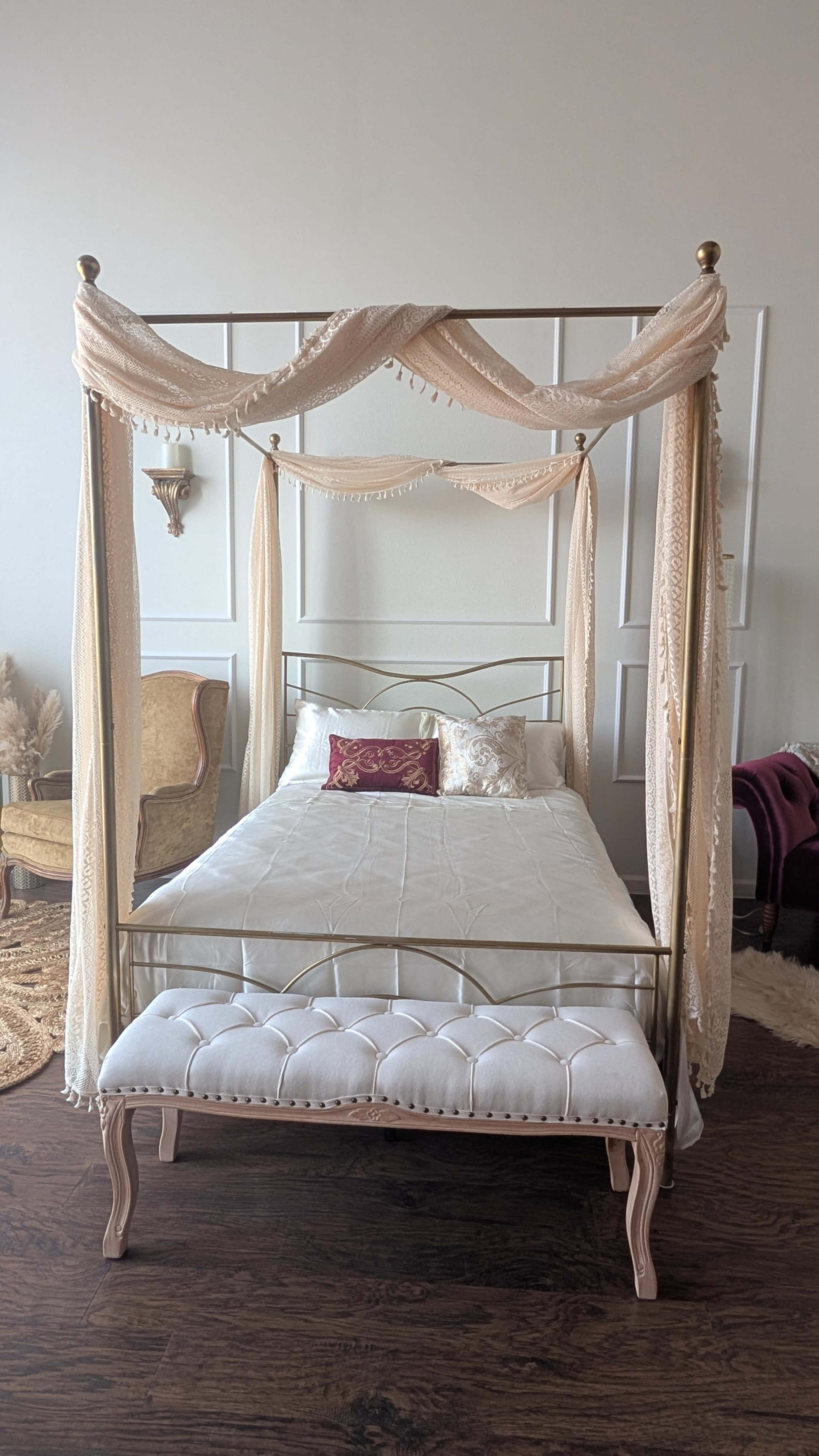 The image shows a four-poster bed with draped fabric and decorative pillows, positioned in a room with elegant furnishings.