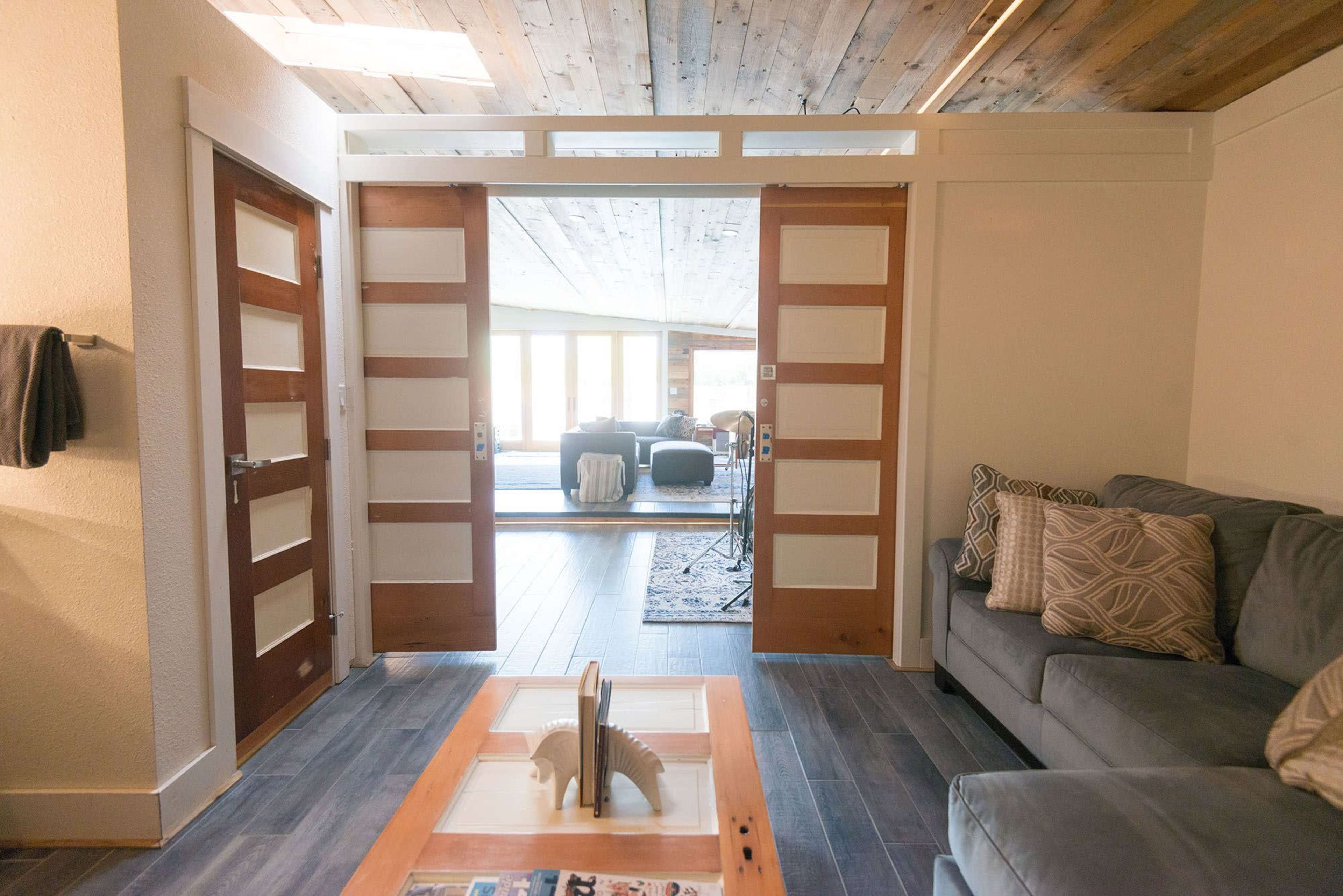 The image shows a modern interior space featuring an open doorway with double doors, a gray sofa, and wooden flooring.