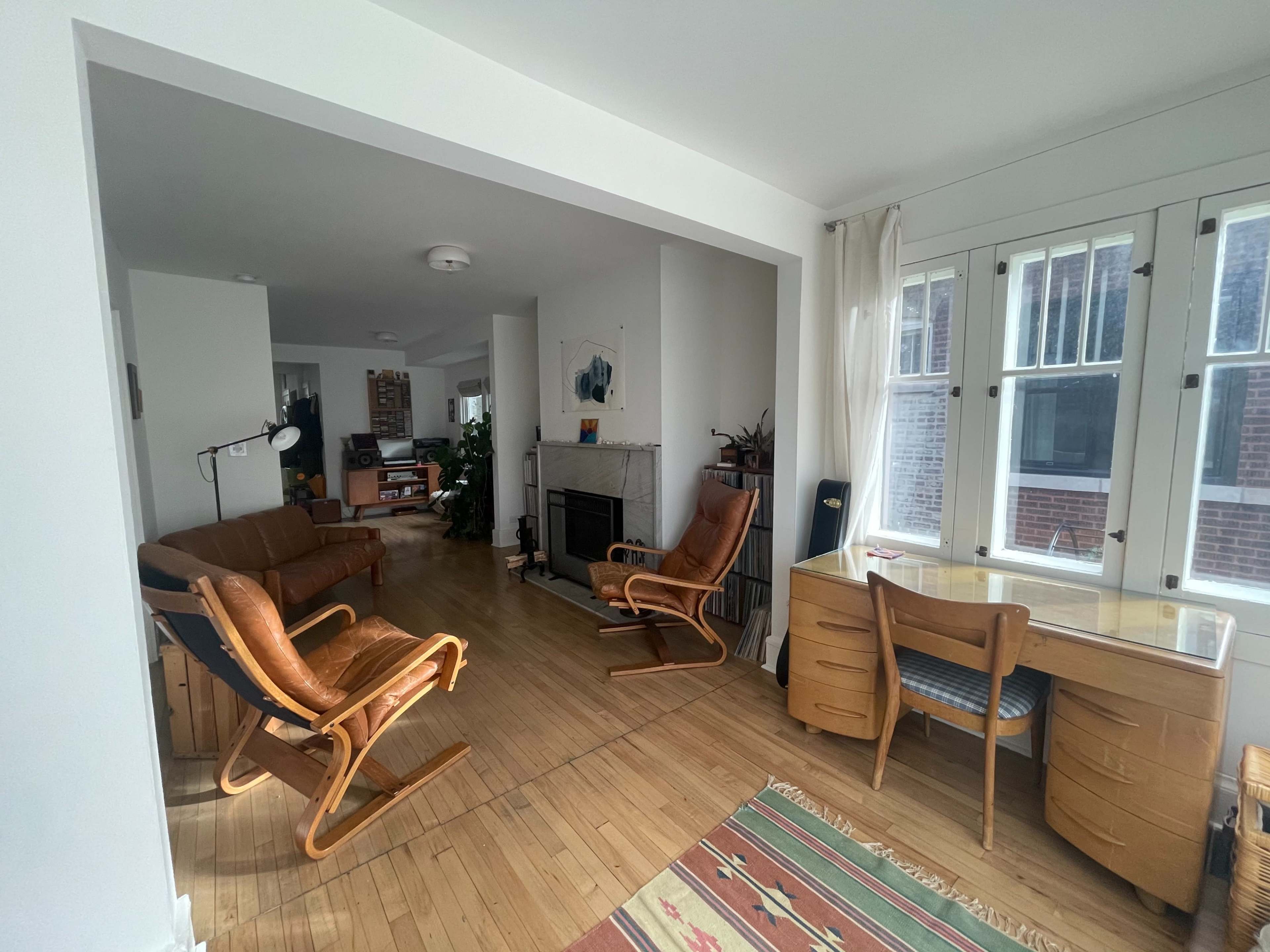 A bright, open living space featuring a leather sofa, two rocking chairs, a desk, and a fireplace.