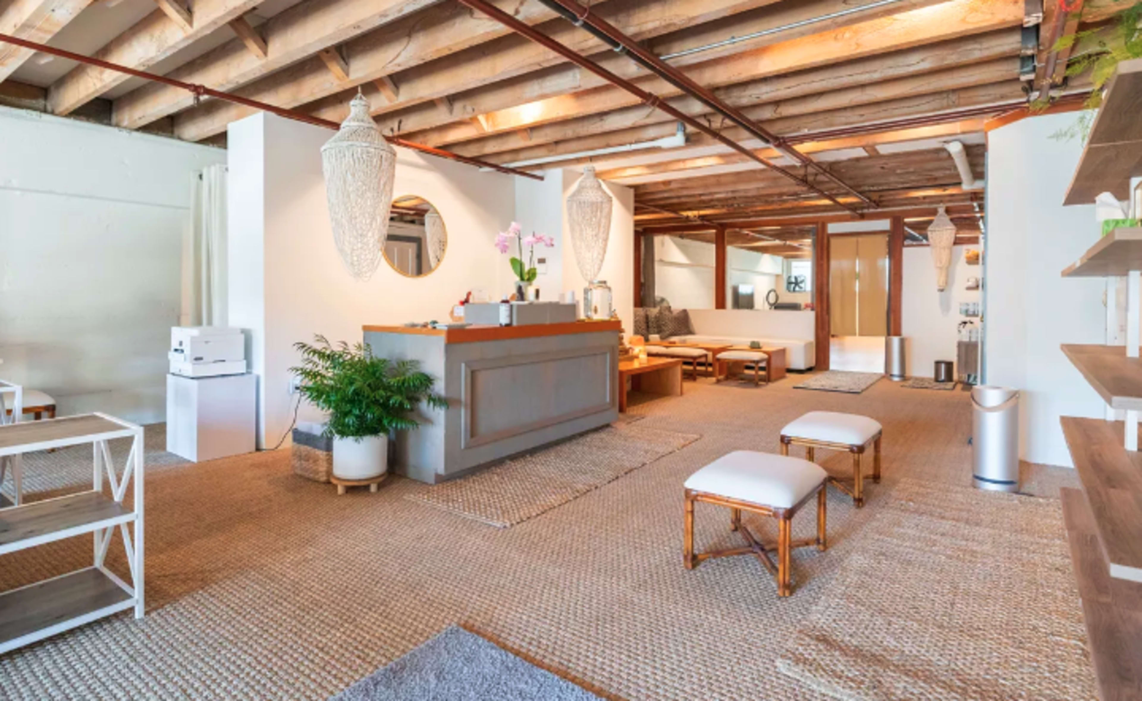A spacious, modern interior with wooden beams, a reception area, and a lounging space furnished with minimalist seating and decorative plants.
