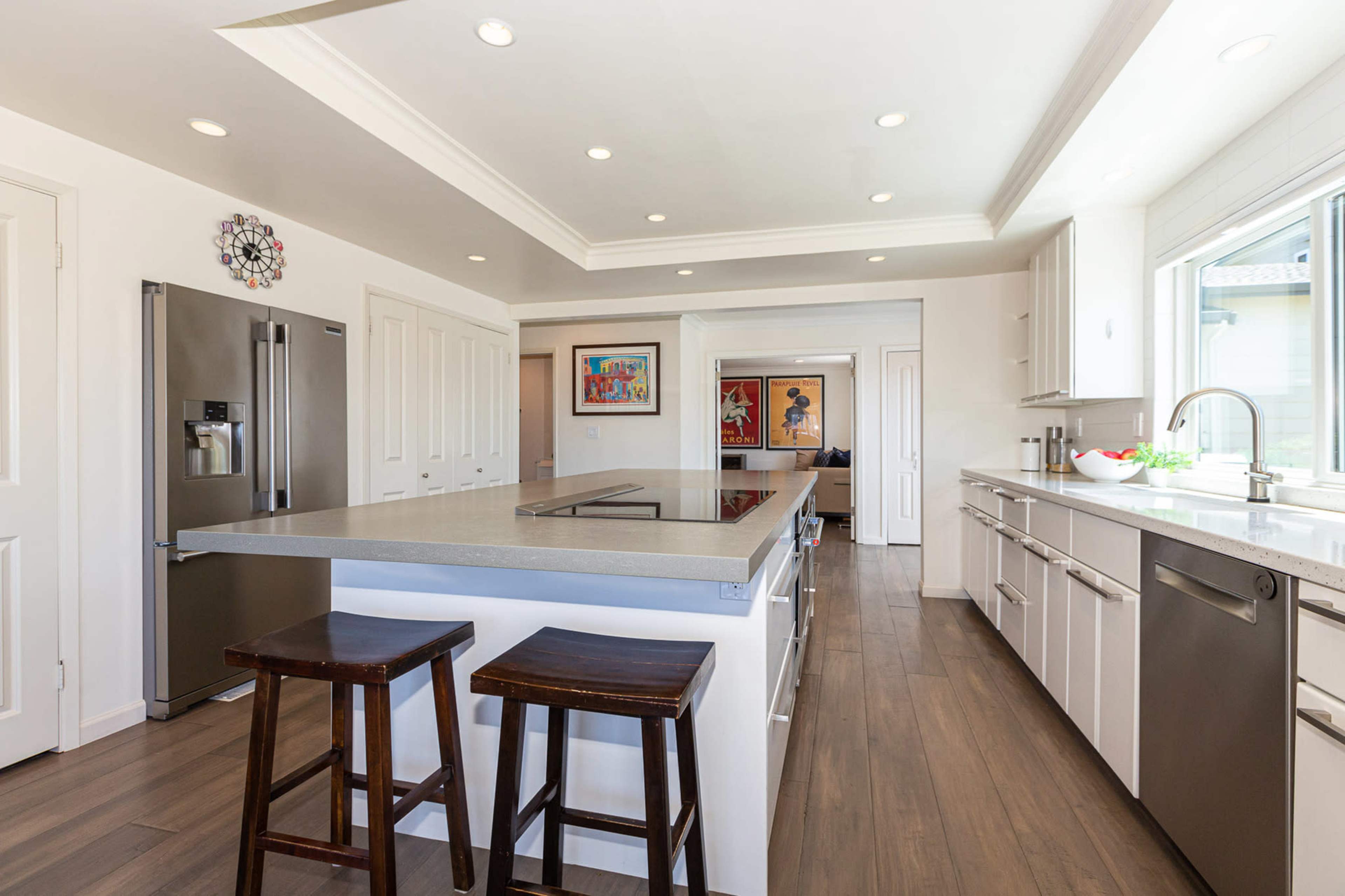 A modern kitchen features a central island with two wooden stools, stainless steel appliances, and ample counter space.