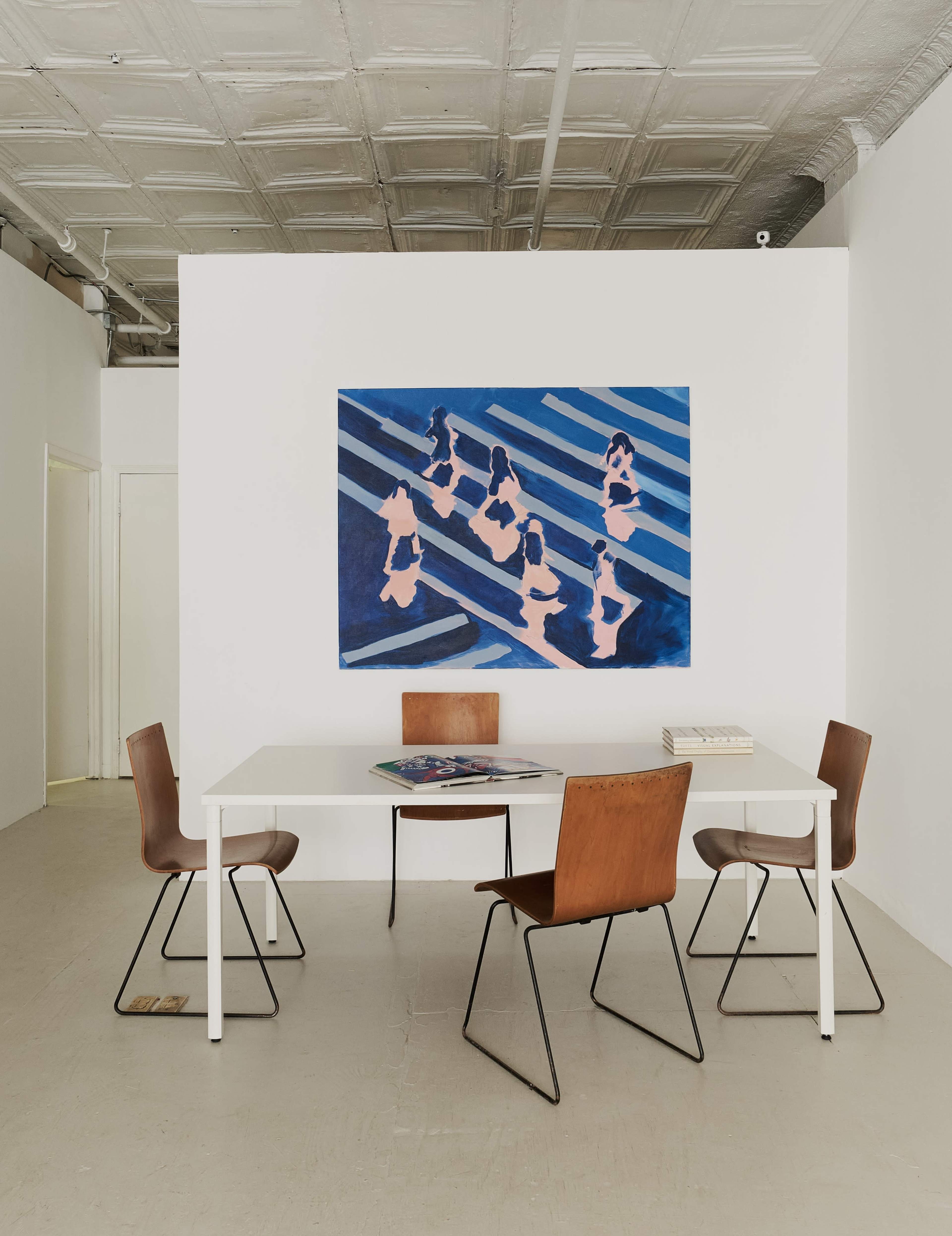 A minimalist interior features a white table surrounded by four chairs, with a large blue and pink abstract painting on the wall.