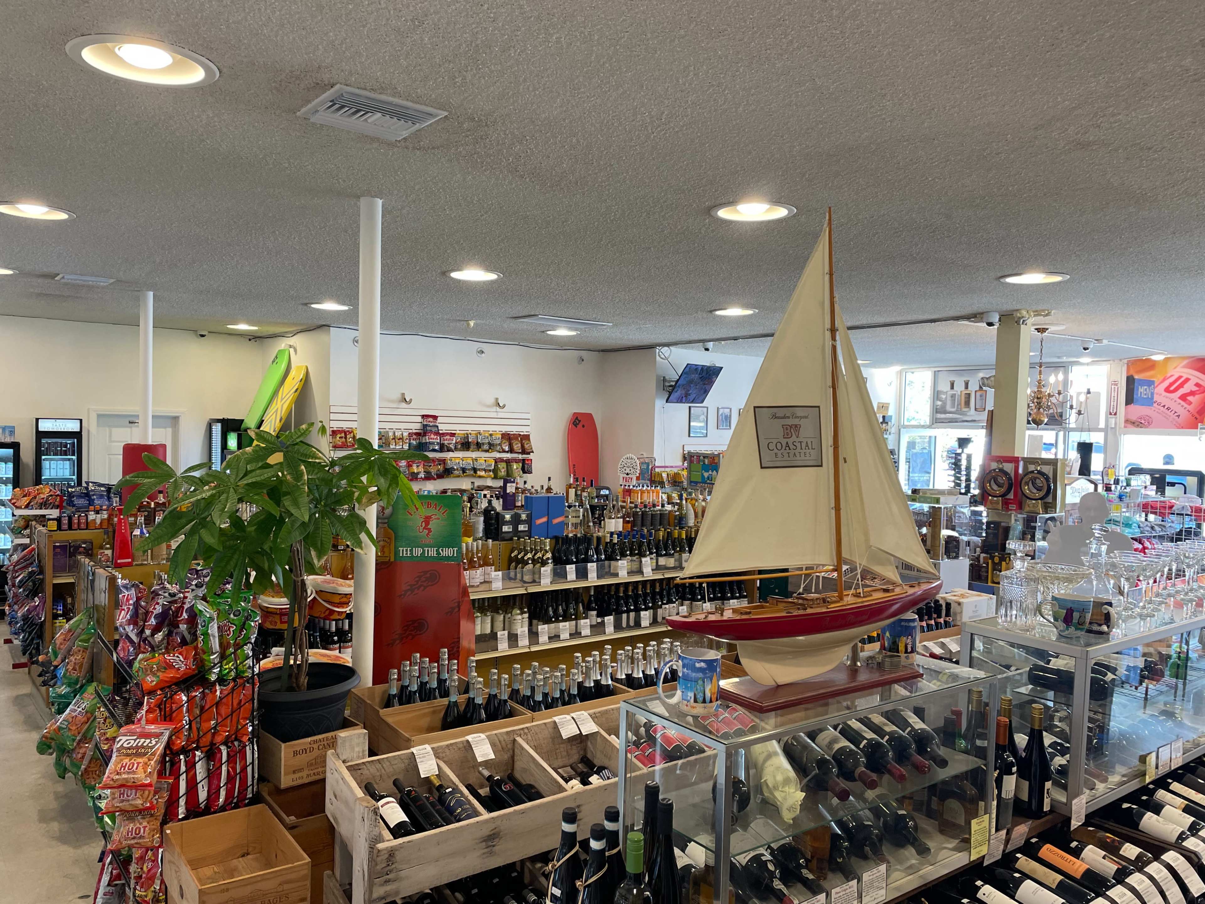 The interior of a convenience store showcases shelves filled with various beverages, snacks, and a decorative sailboat in a display case.