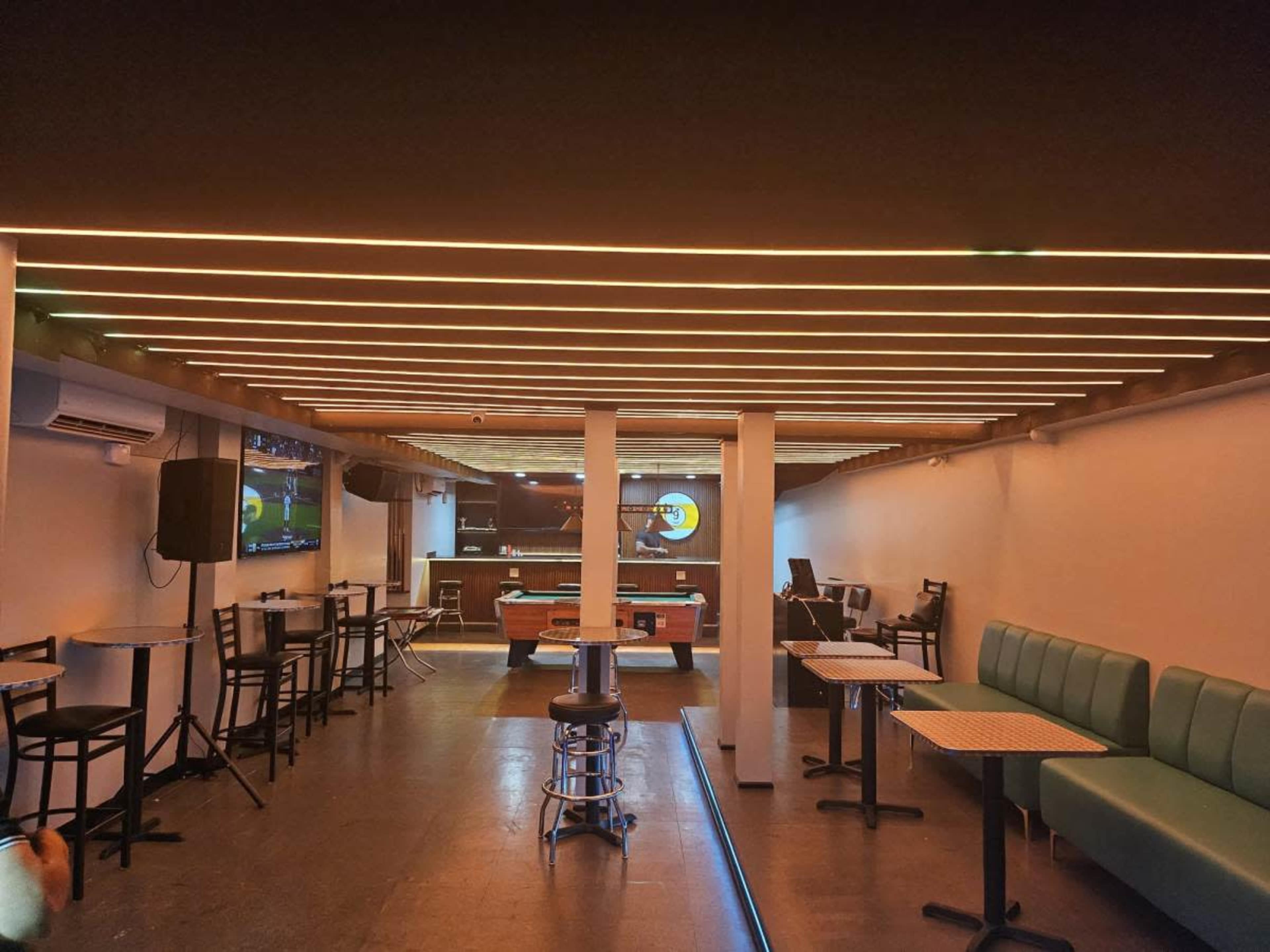 The image shows an empty bar area with a pool table, seating booths, and a television mounted on the wall.