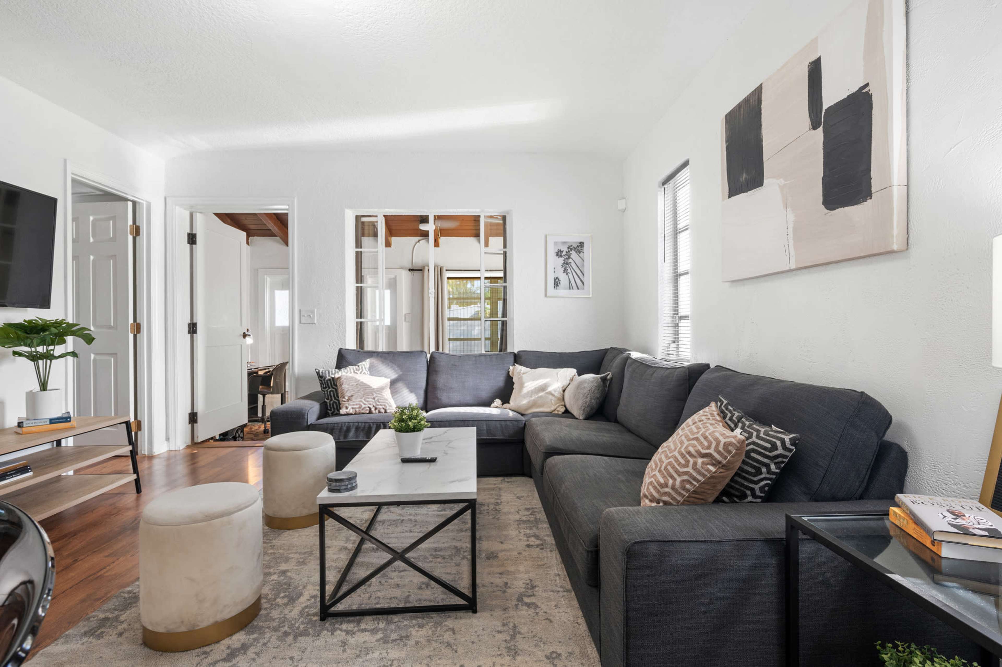 A living room with a dark gray sectional sofa, a coffee table, and light-colored stools arranged around a light-colored area rug.