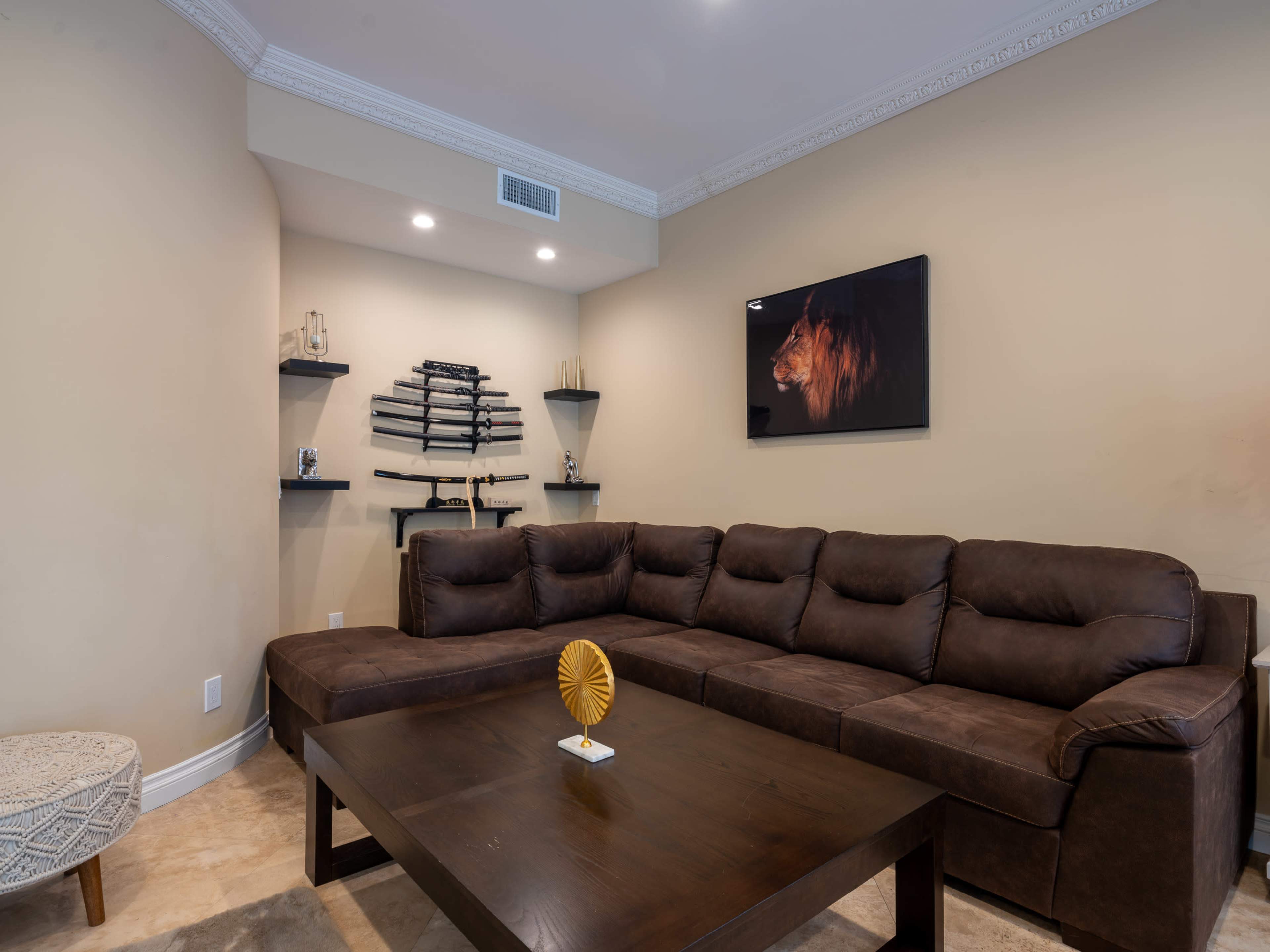 The image shows a cozy living room with a brown sectional sofa, a wooden coffee table, and decorative shelves displaying various items, along with a framed artwork of a lion on the wall.