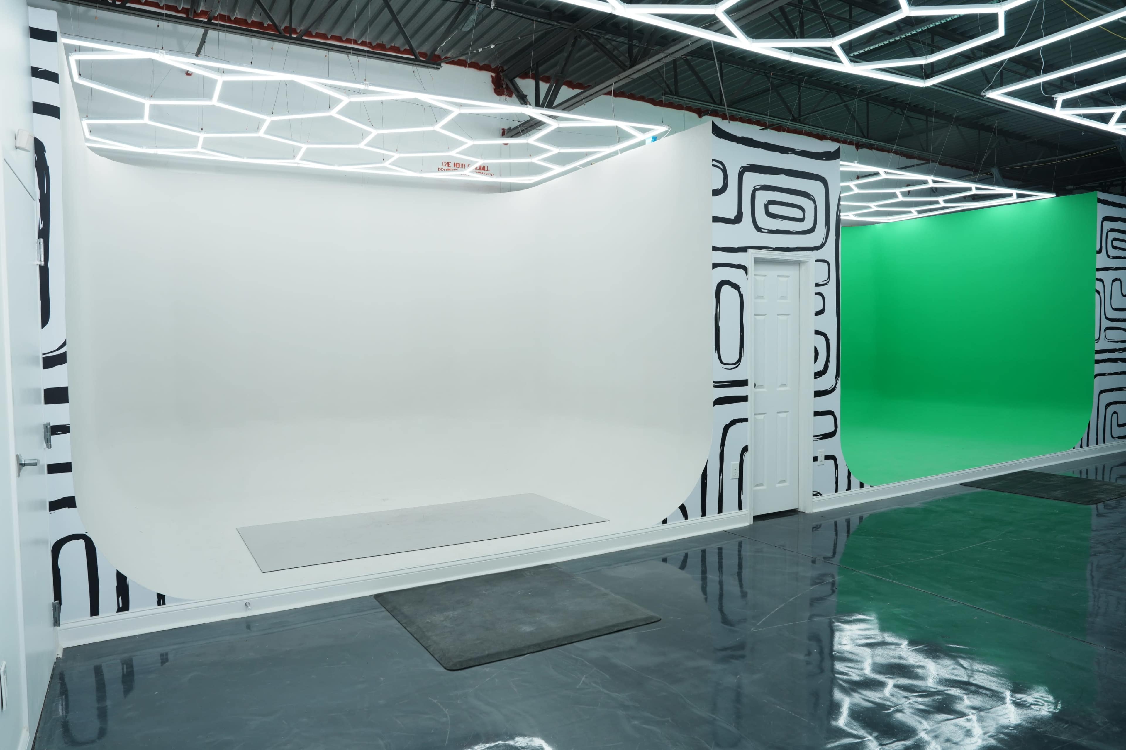 The image shows a spacious studio with two photo backdrops: one white and the other green, framed by modern lighting fixtures.