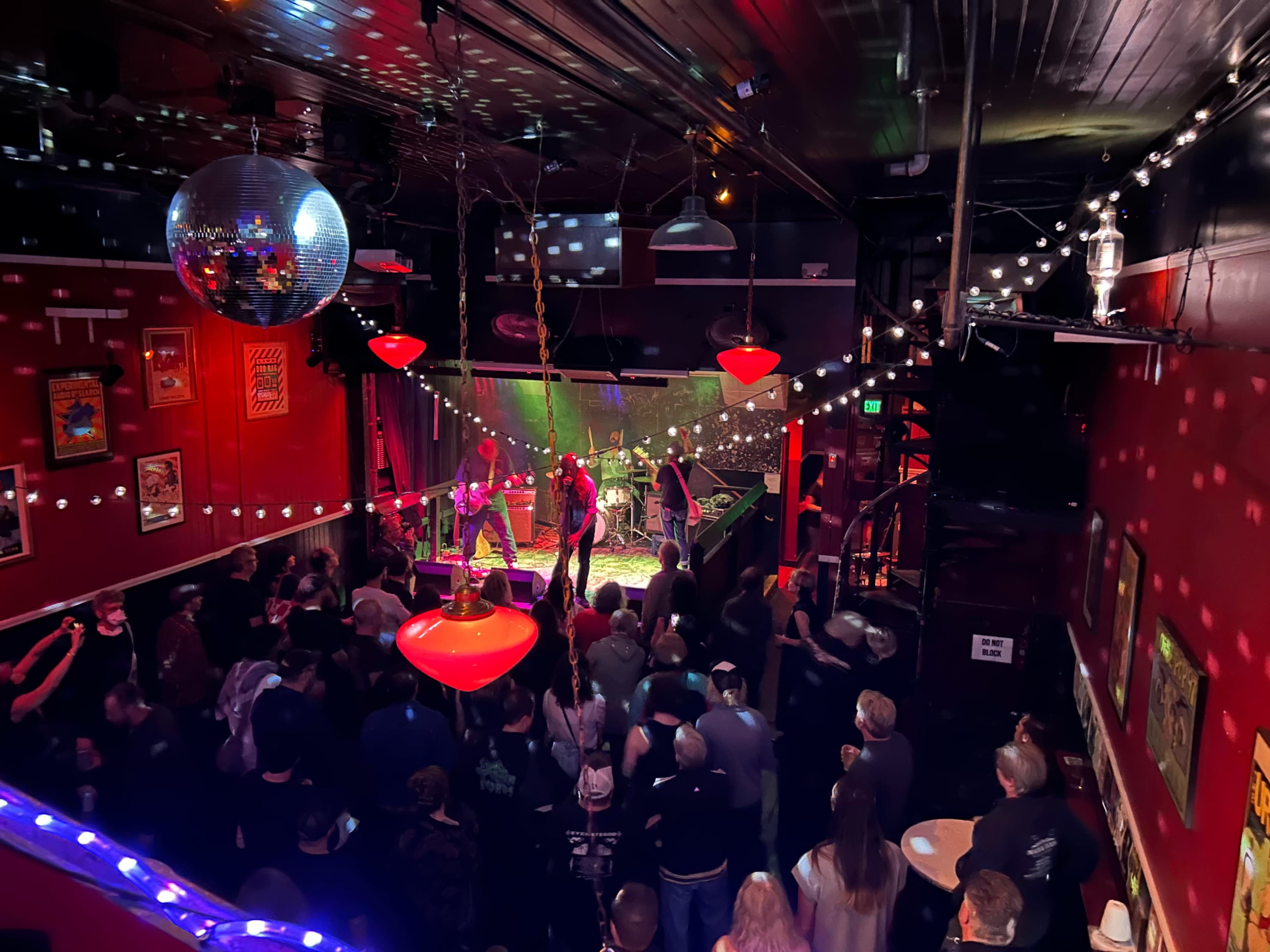 A crowd watches a live performance on stage in a dimly lit venue adorned with colorful lights and decorations.